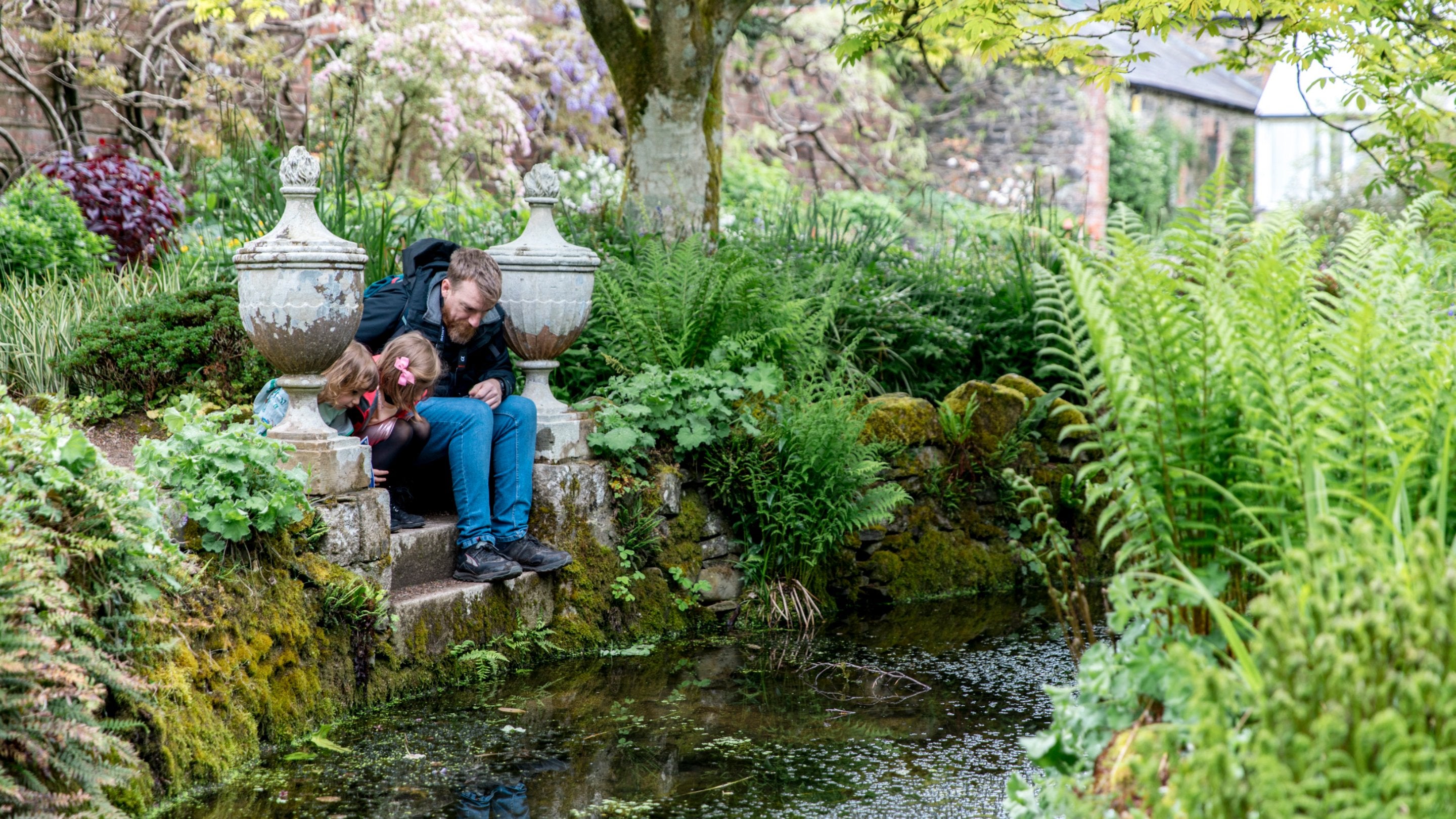 An adult and child sitting on stone steps next to a small stream, surrounded by lush foliage