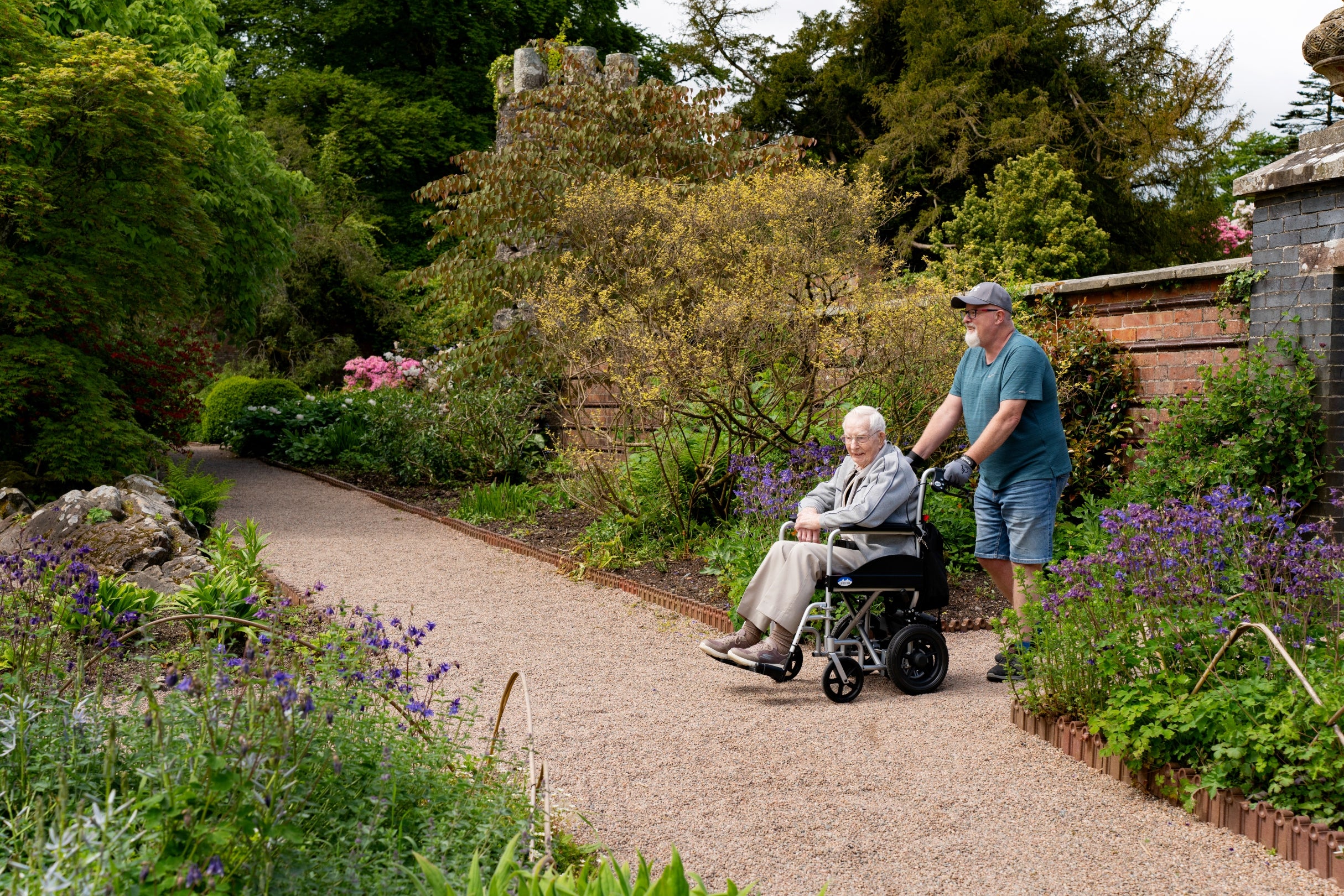 A wheelchair user takes in the Walled Garden on a sunny day with their companion at Rowallane Garden
