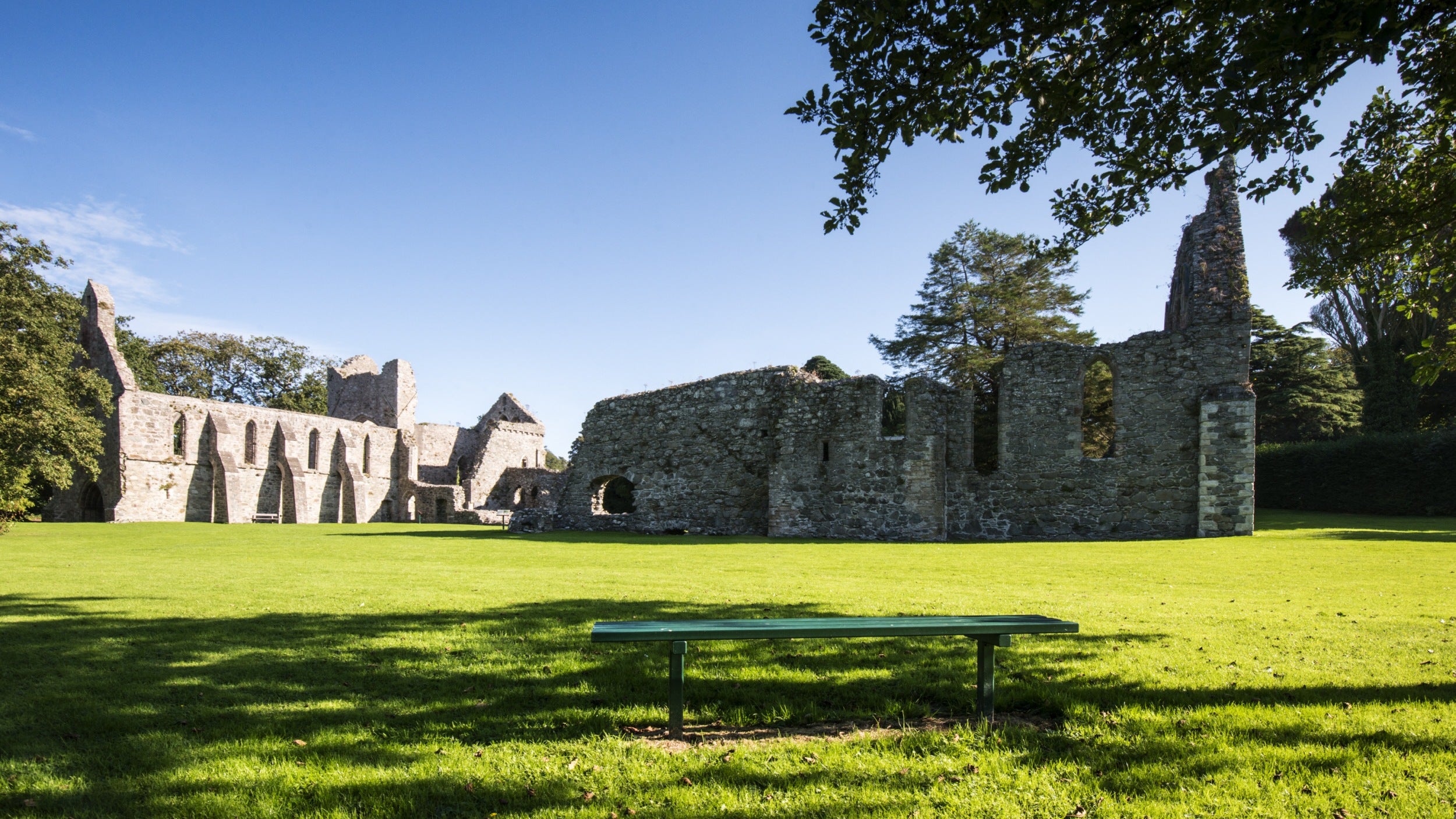 Exterior view of the ruins of the Cistercian priory Grey Abbey, County Down, with a grassy lawn and bench in the foreground