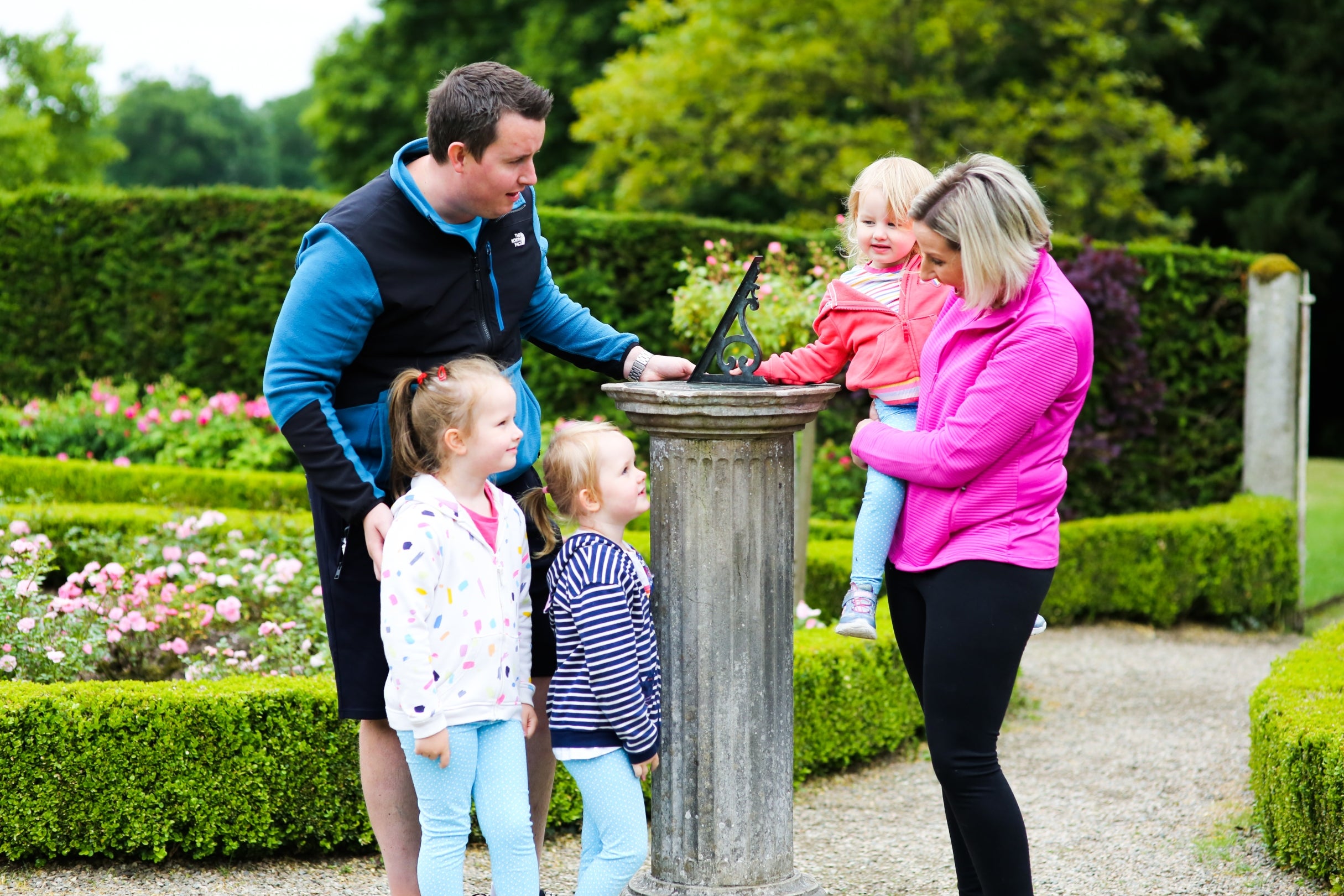 A family of five have stopped to admire the sundial in the rose garden