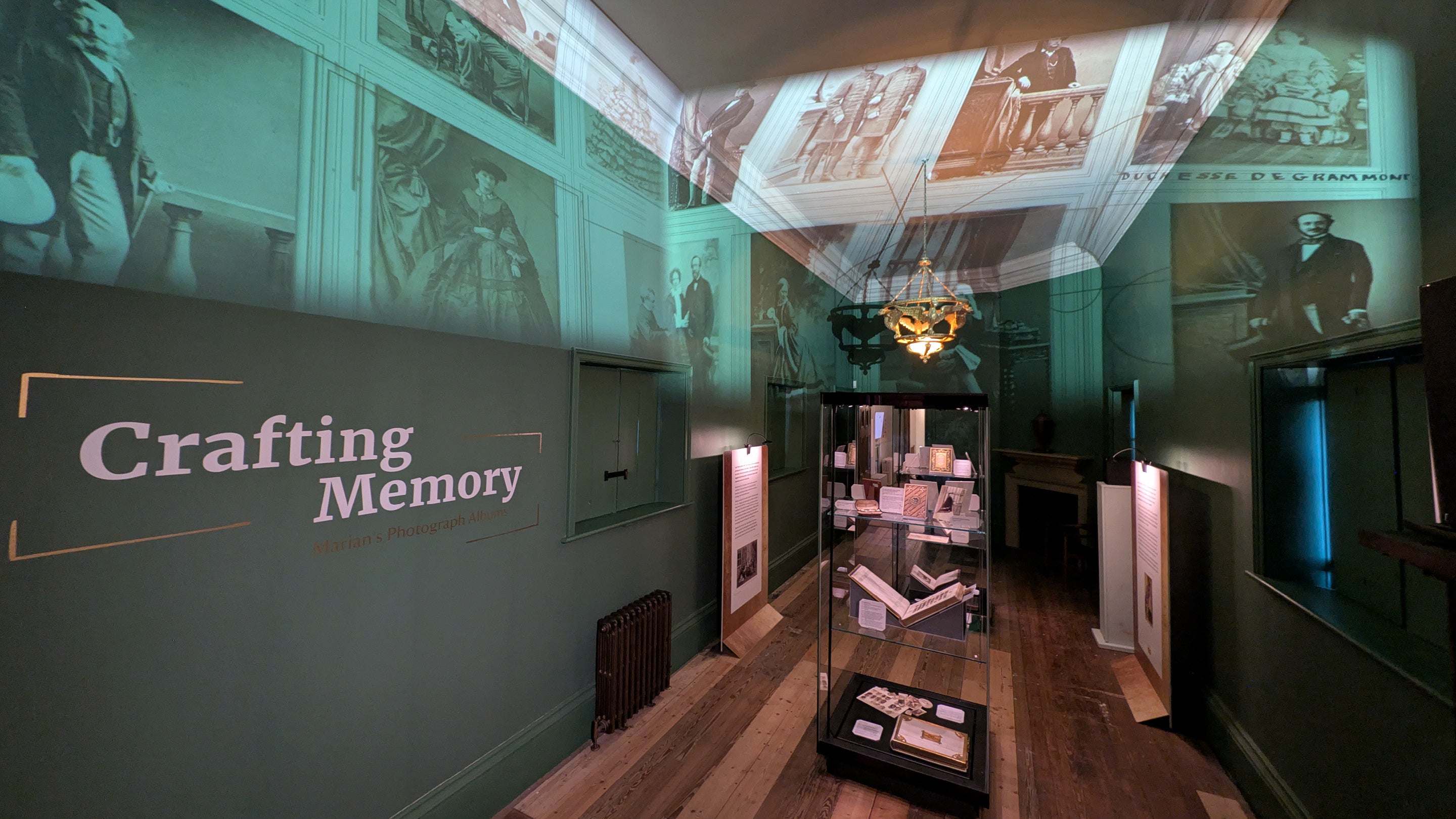 The Crafting Memory exhibition at Belton Estate with photographs projected on the walls and ceiling and display cases with albums inside.