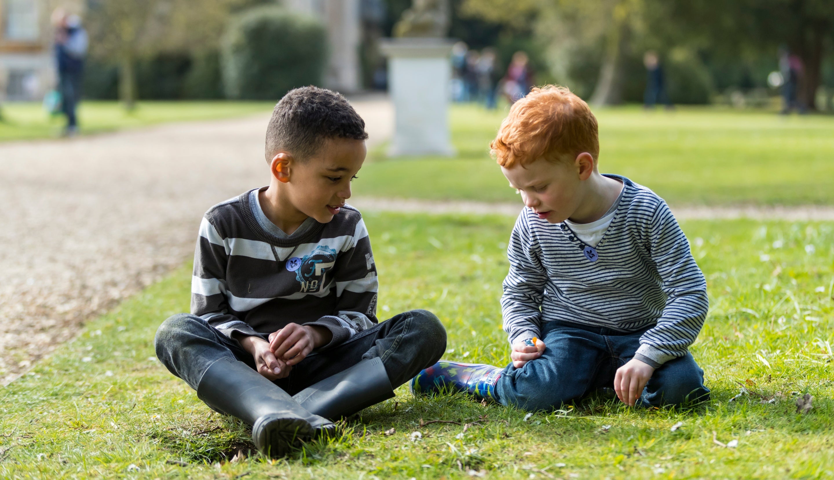 Children sat down on the grass in front of Belton House, playing with daisies