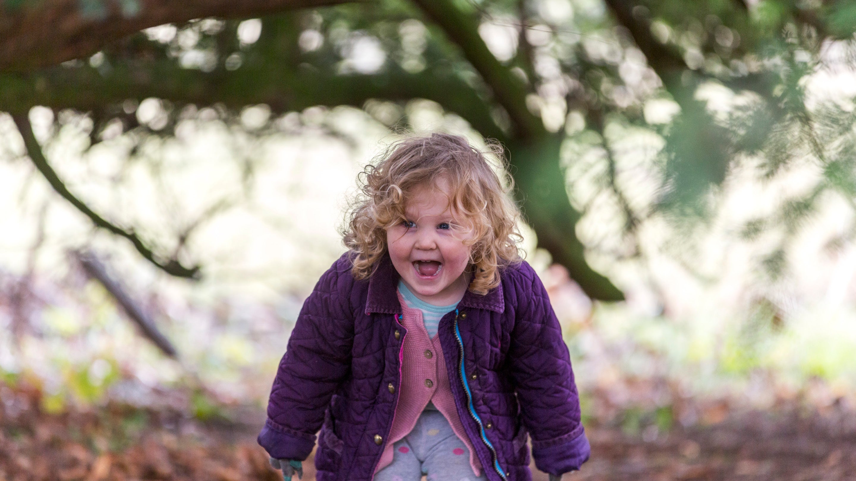 A little girl wearing a purple jacket screams in excitement in a woodland setting.