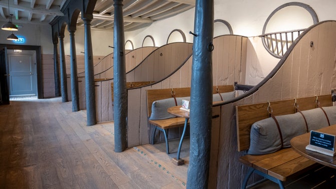 Seating at Belton's Stables Café with long wooden bench-style seating with a backrest from which a long grey cushion is suspended.