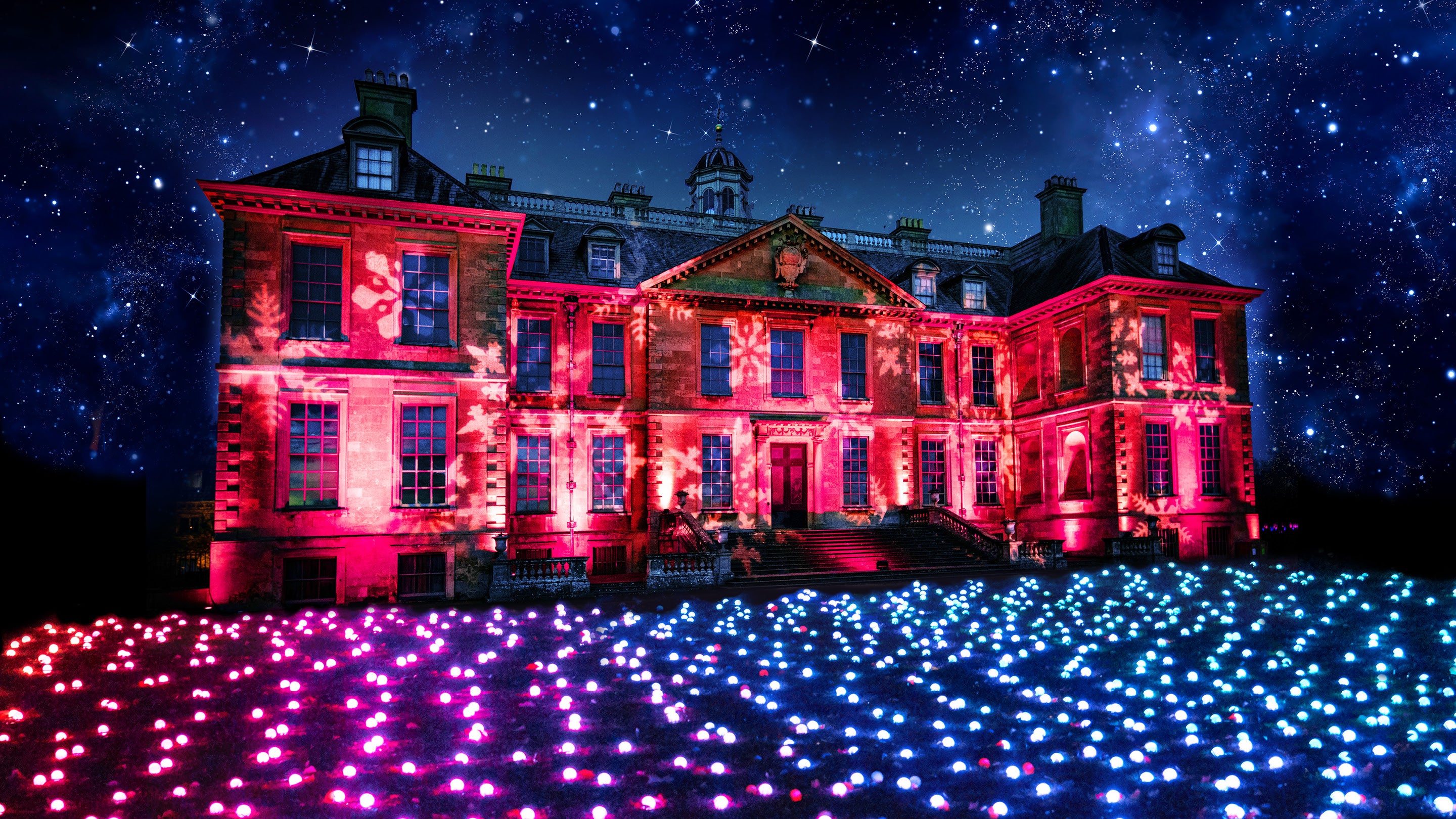 Belton House with red lighting and snowflakes projected onto it. There are small globes of light on the grass in front of it in ombre colours from red to white, blue and green.