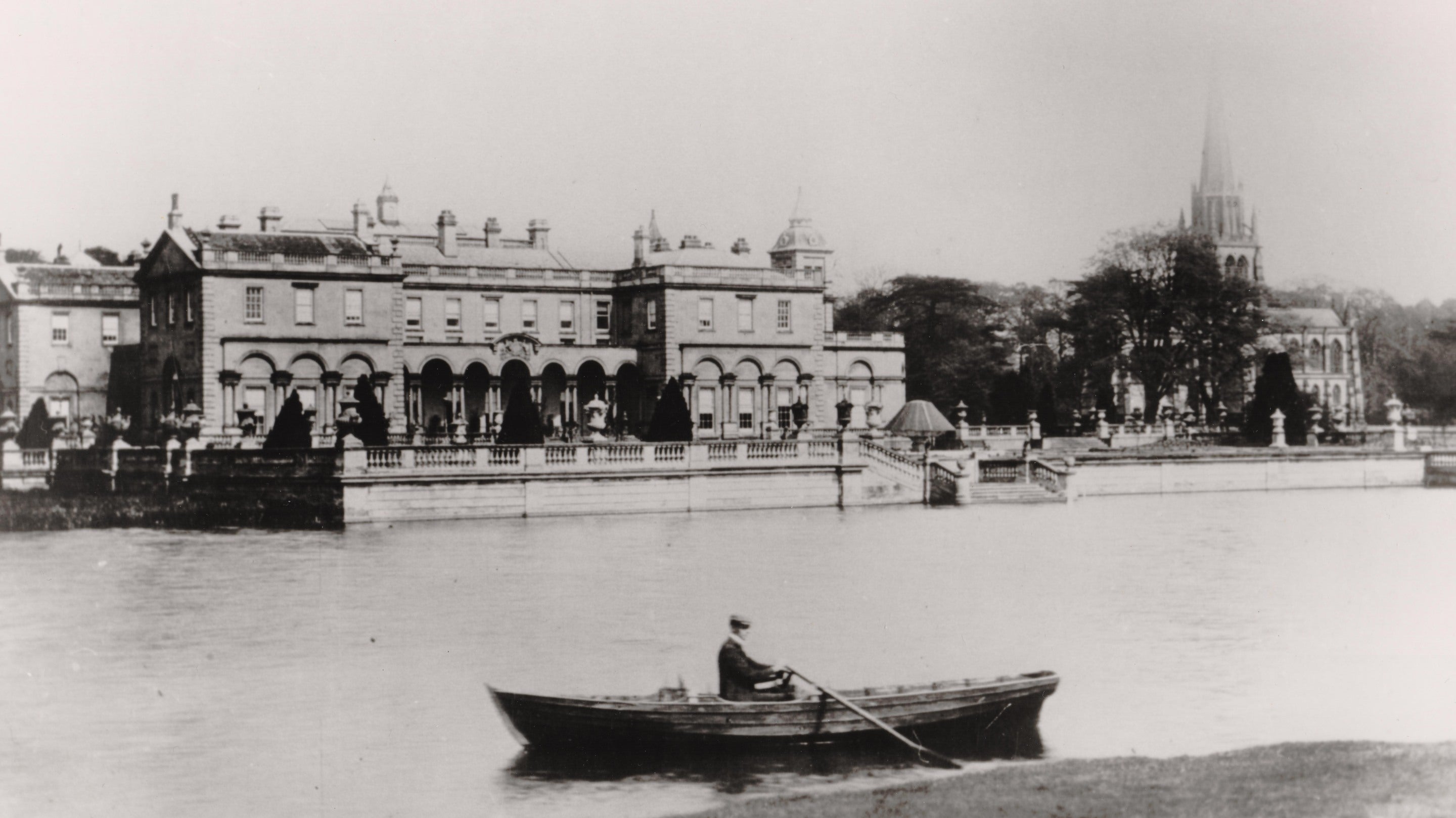 Looking across the lake to Clumber House and the Chapel. A man is rowing in a boat on the lake