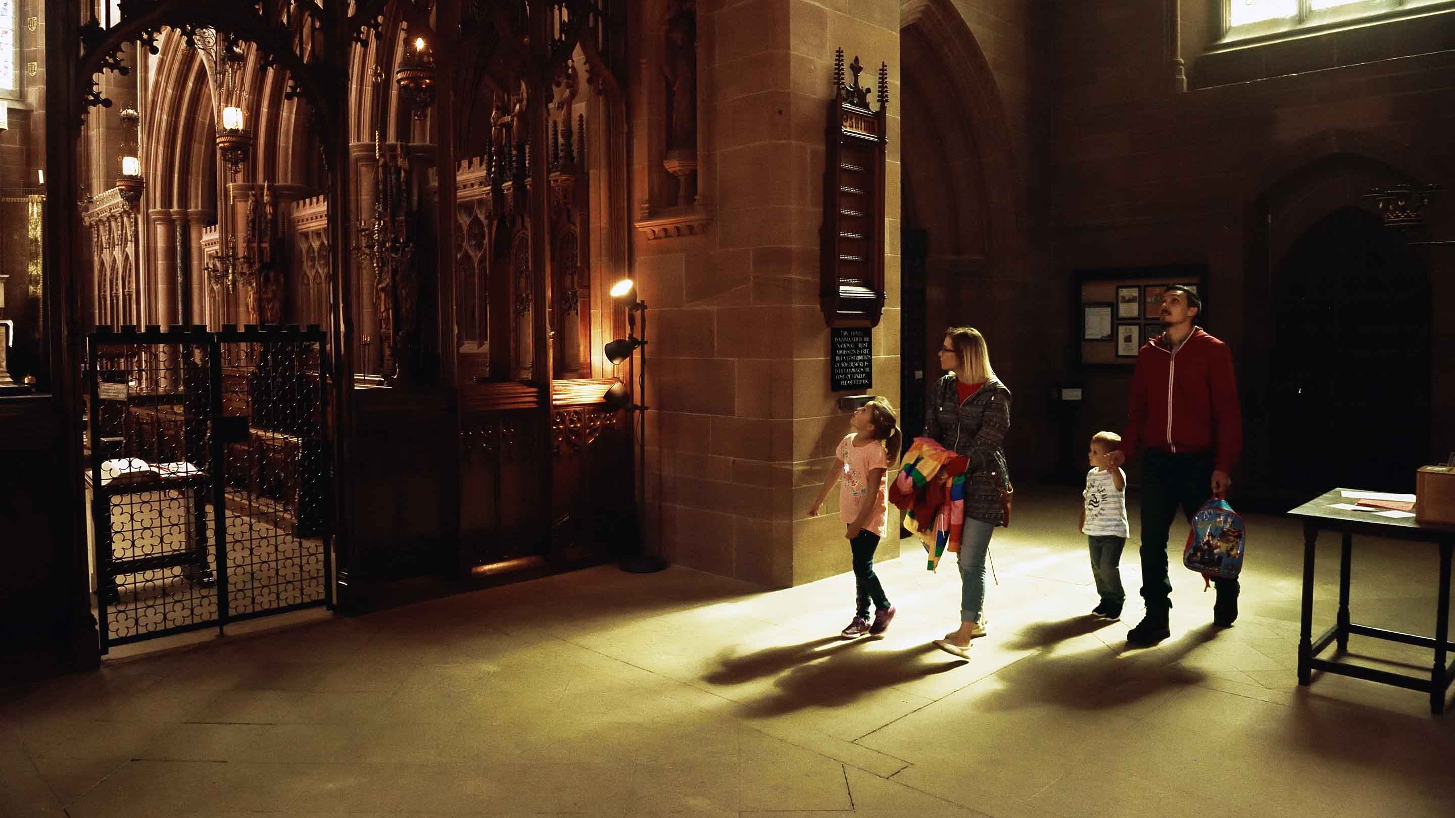 A family of two adults and two young children looking up at the archway leading to an ornately-gated area inside the Chapel of St Mary the Virgin at Clumber Park, Nottinghamshire.