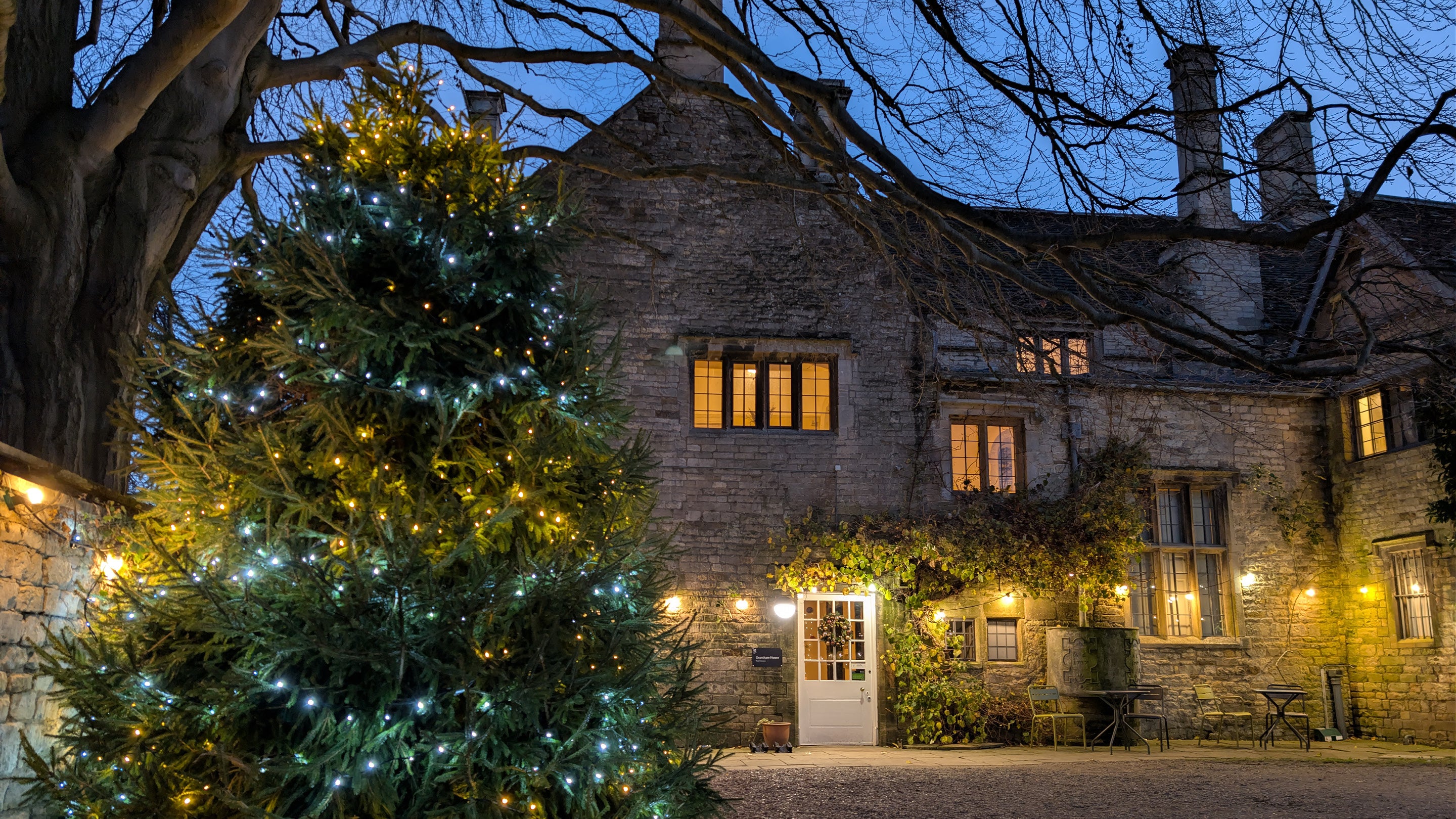 Grantham House at Christmas with golden lights strung along its façade and a huge Christmas tree with blue and gold lights to the left in the courtyard.
