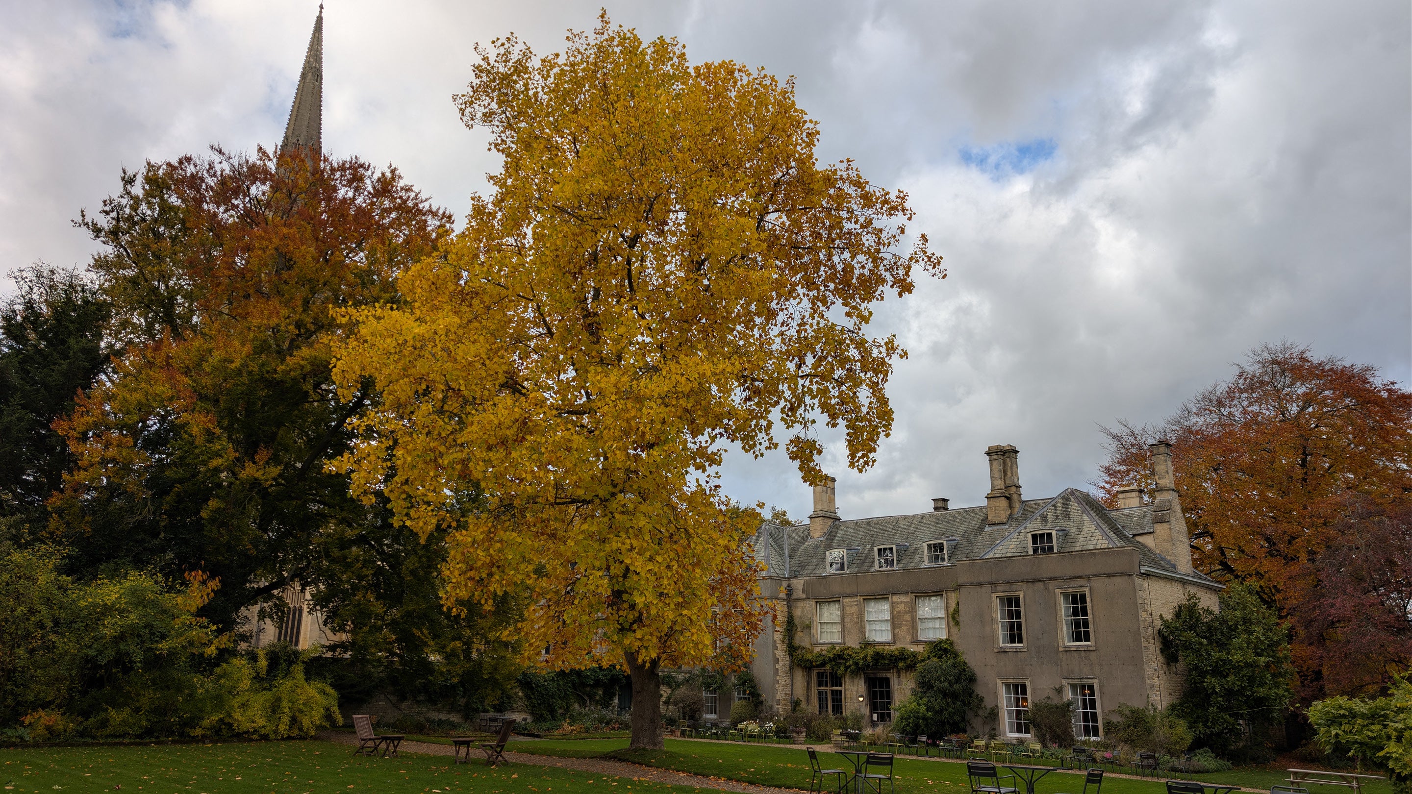 A view of Grantham House from the upper lawn in autumn. Trees frame the house with orange and gold and the spire of St Wulfram's church can be seen on the left.