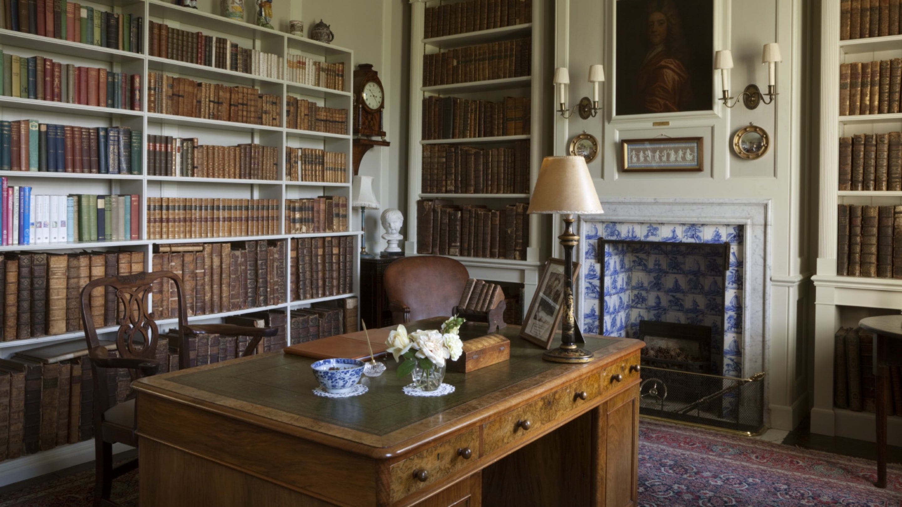 A view inside the Library at Gunby Hall, with a writing desk covered and chair in the foreground and bookcases containing leather-bound books lining the walls