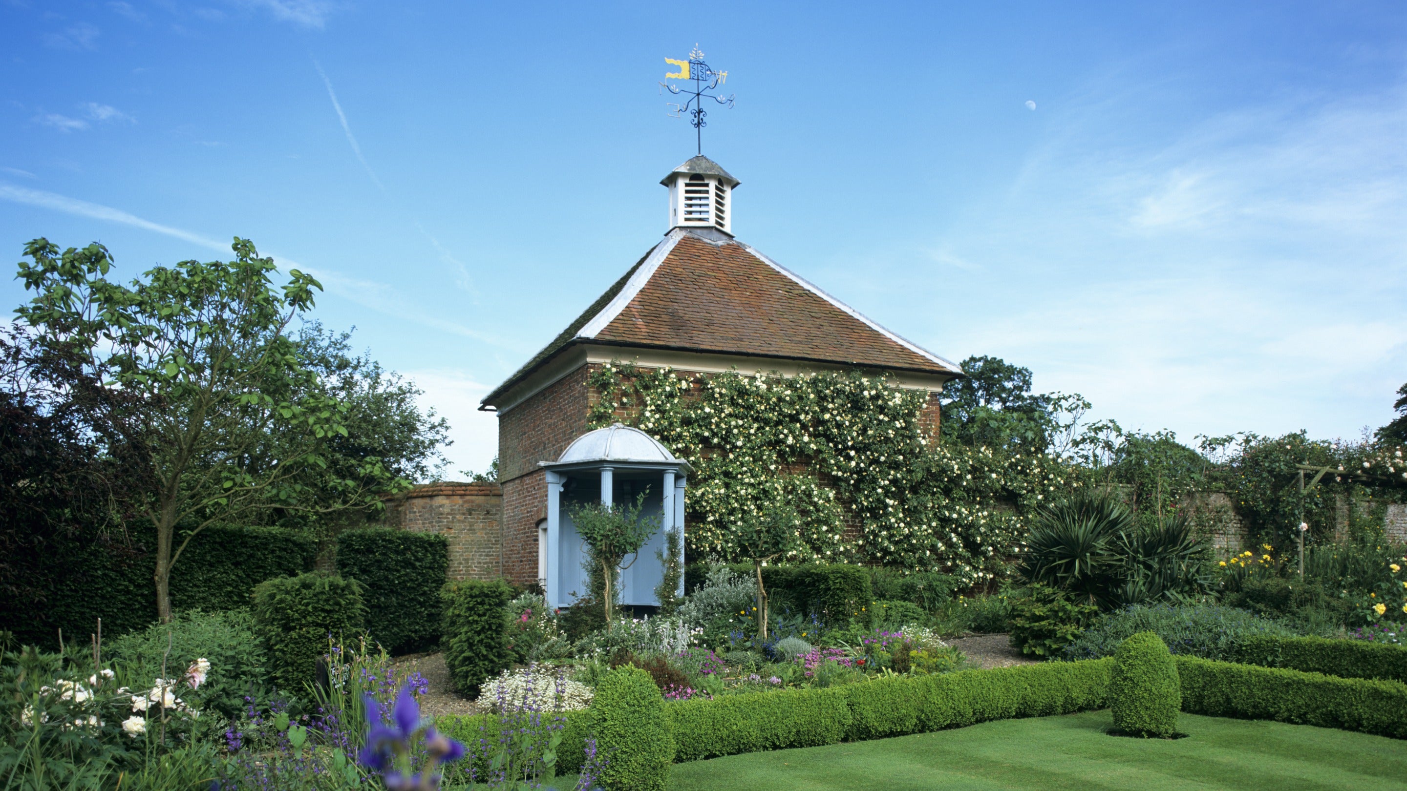 A blue wooden gazebo overlooking Gunby’s formal gardens, surrounded by flowers and clipped hedges.