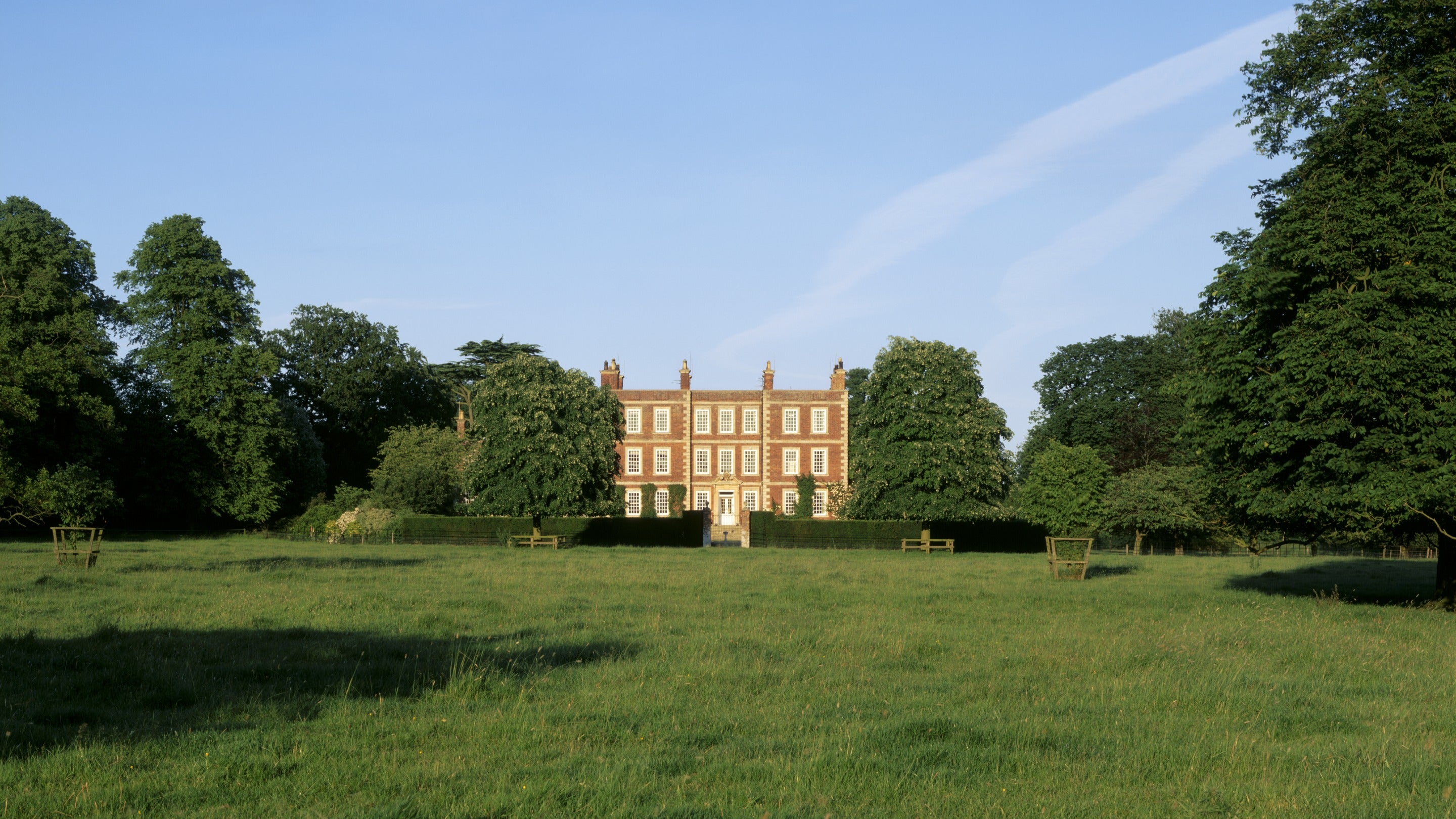 View from the parkland towards Gunby Hall, framed by mature trees beneath a clear evening sky.