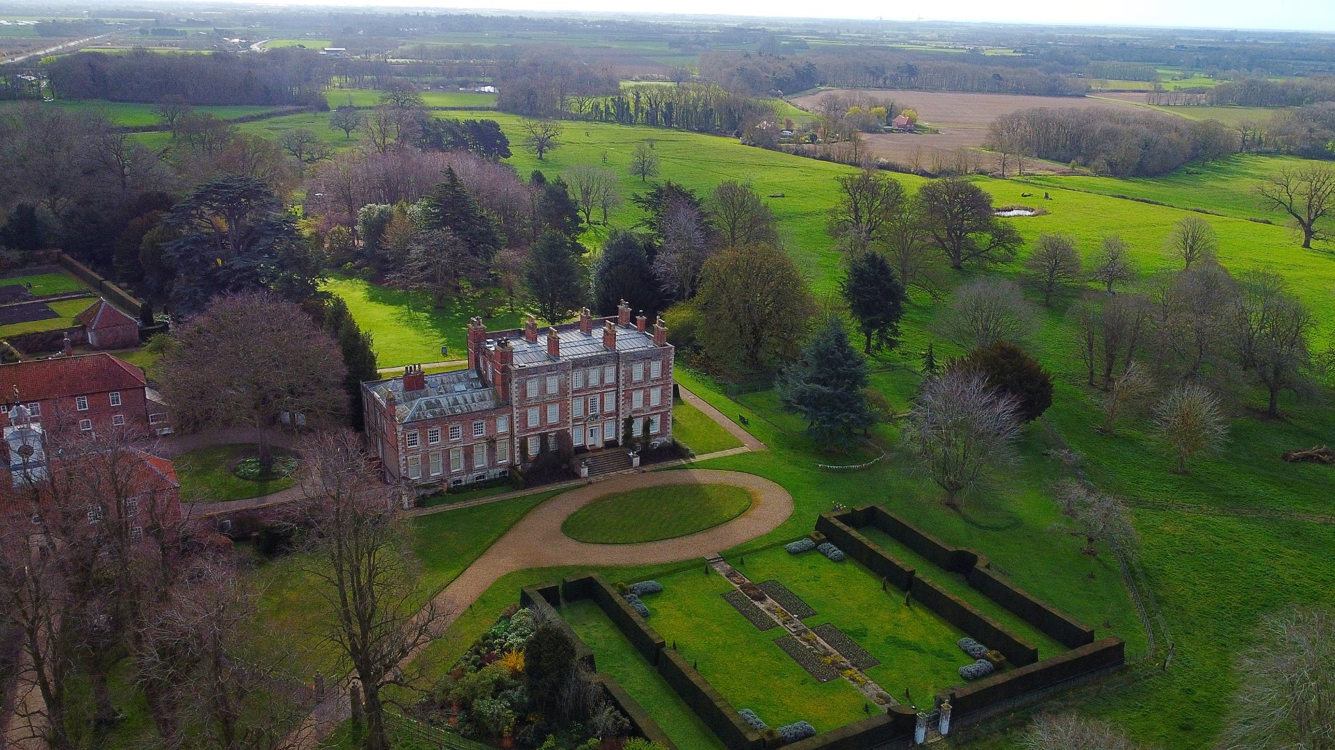 A view of Gunby Hall from above with the gardens in the background and miles of countryside stretching out to the horizon