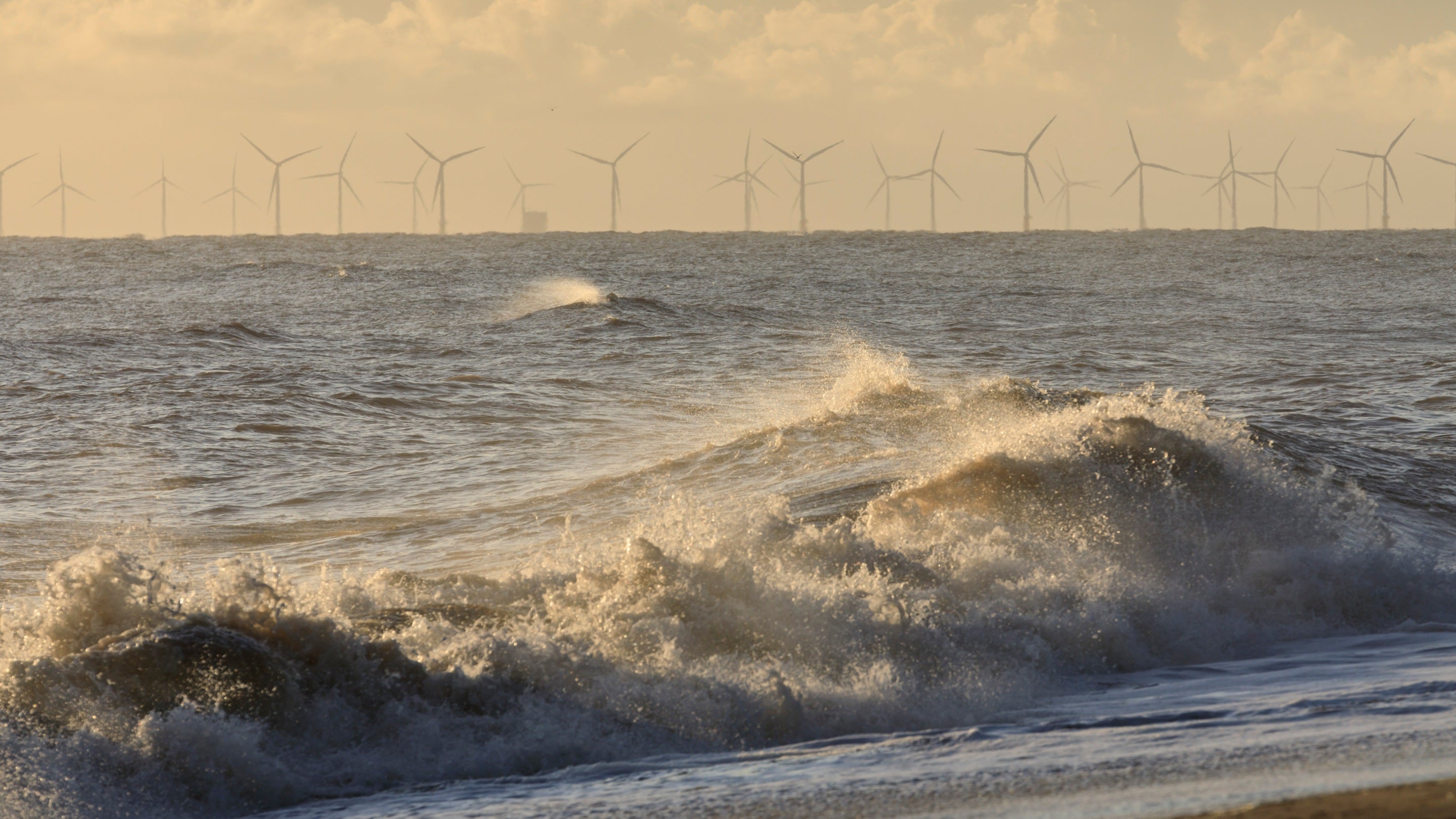 Waves crashing on the beach and wind turbines on the horizon at Sandilands, Lincolnshire
