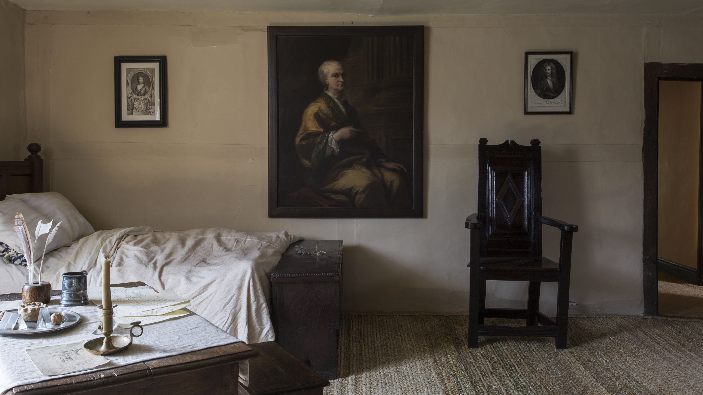 A bedroom at Woolsthorpe Manor, Lincolnshire, with an unmade bed, a desk covered in papers and a portrait of Isaac Newton on the wall