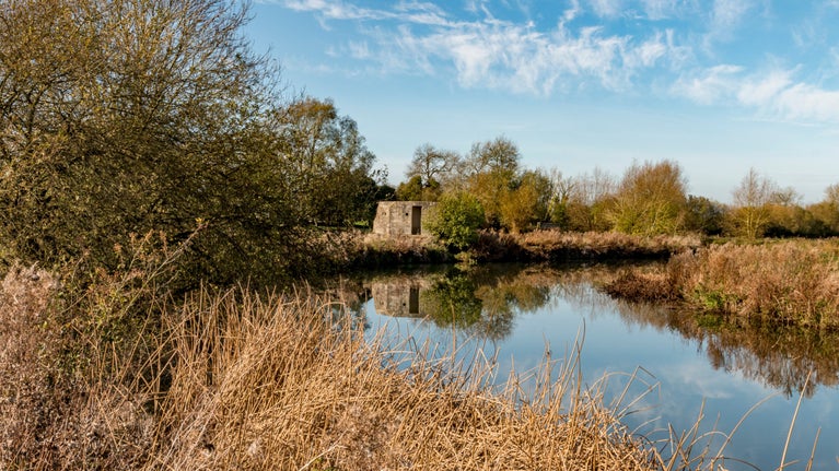 Brick Second World War pillbox beside calm stretch of river and surrounded by reeds and trees