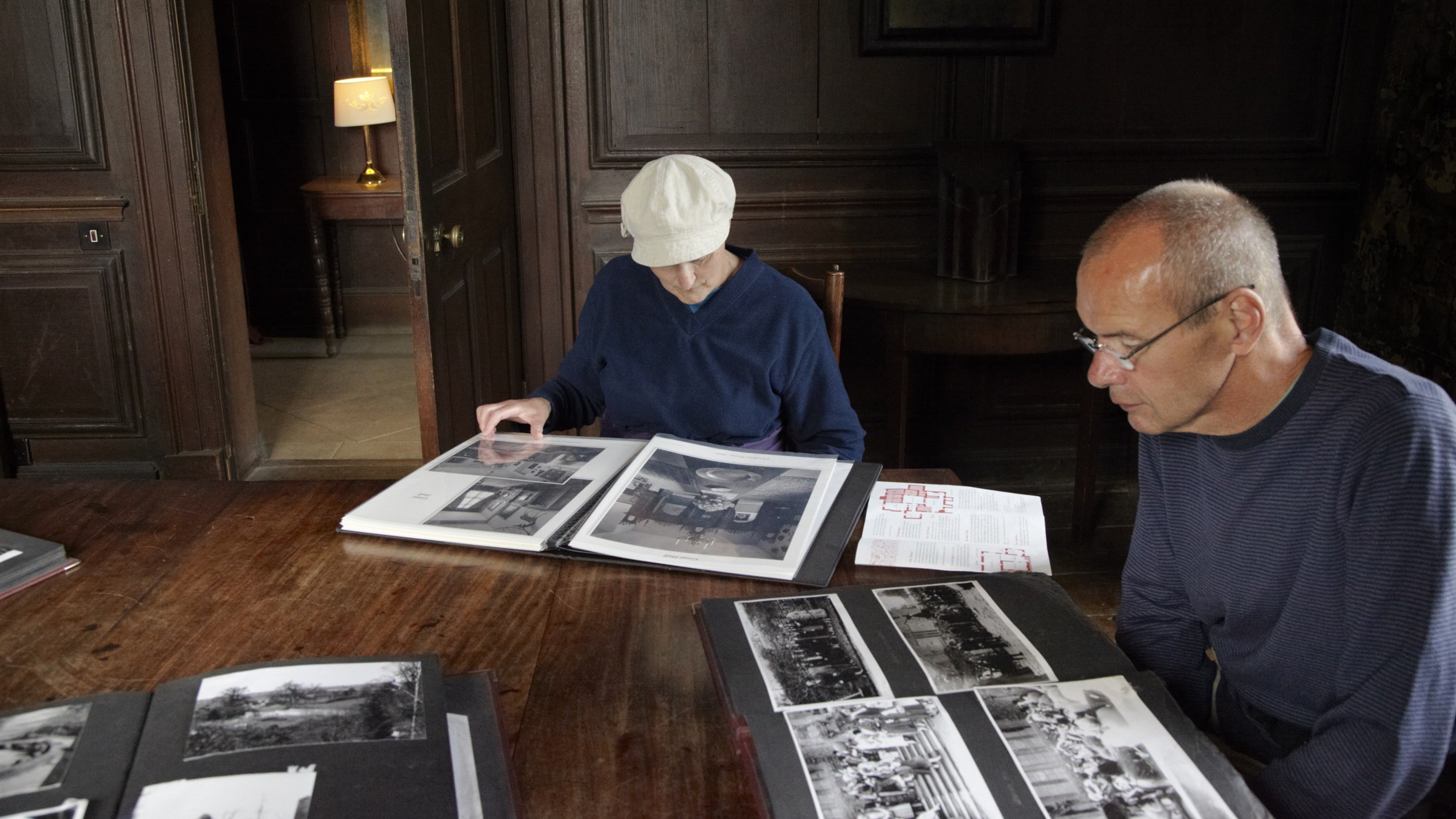 Two people sitting down looking at photograph albums at Chastleton House, Oxfordshire