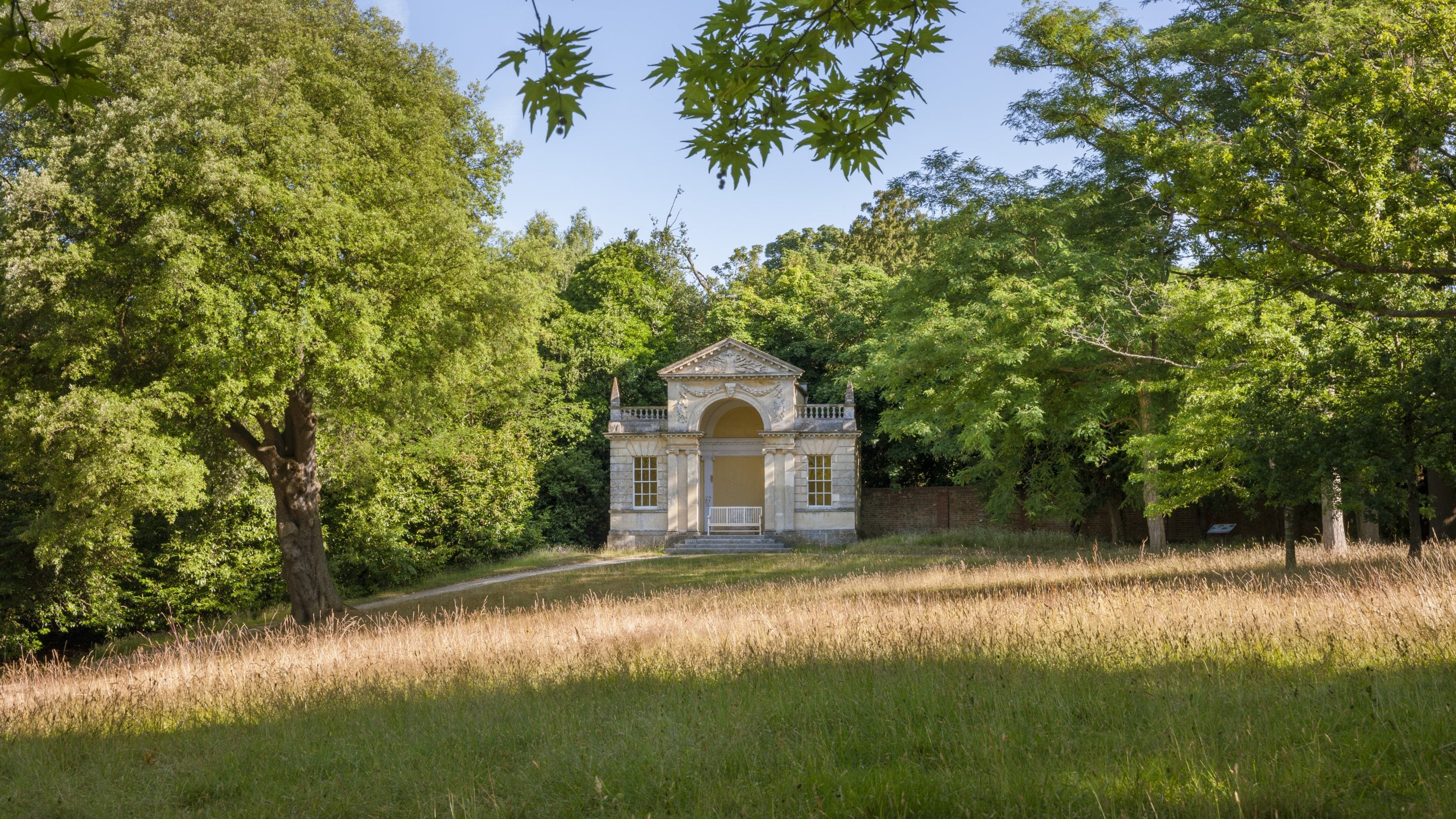 A view across tall grass of the cream stone Blenheim Pavilion at Cliveden in Buckinghamshire