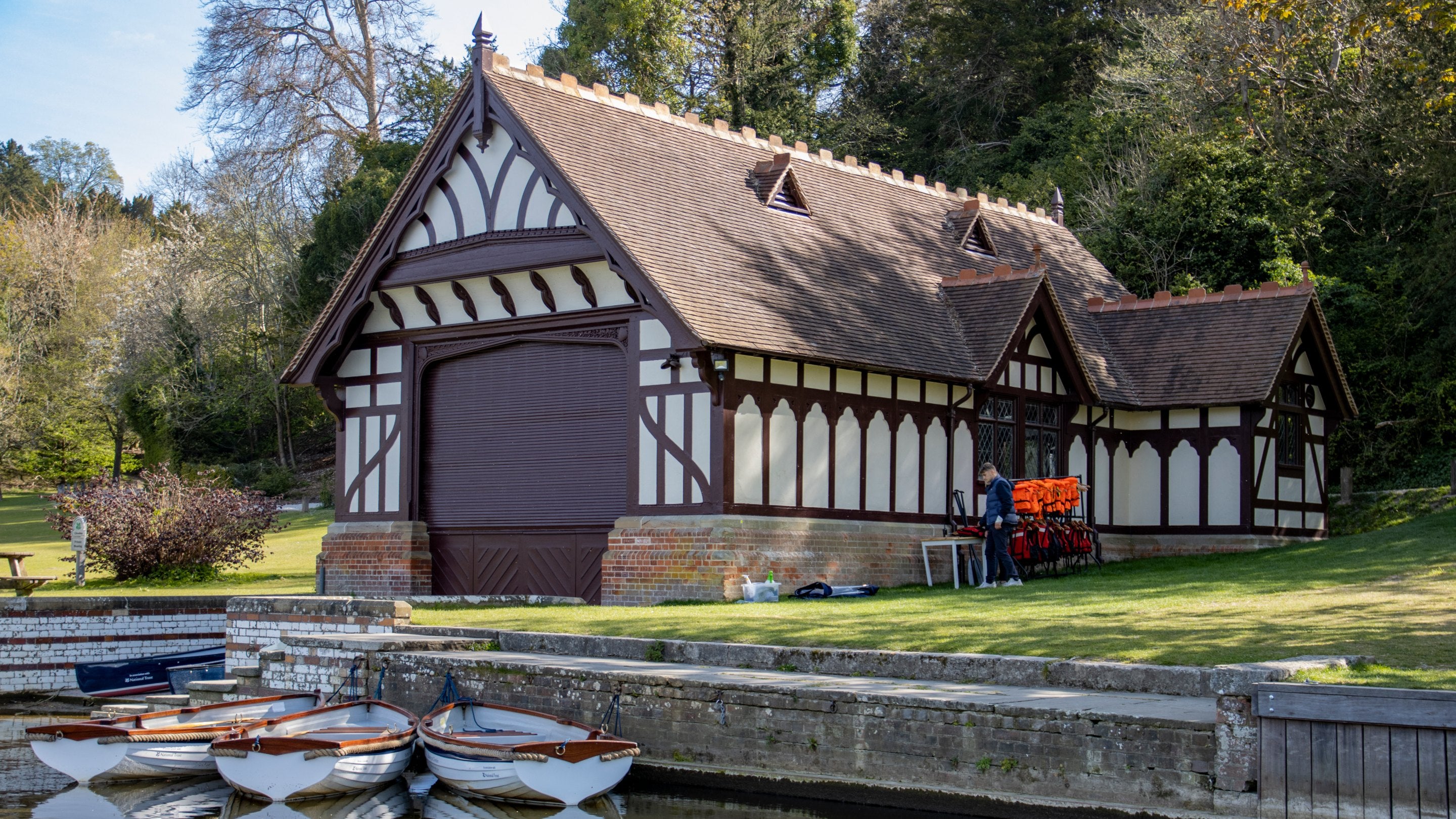 The black and white single storey Boathouse at Cliveden in Buckinghamshire with rowing boats moored outside