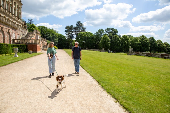 Lady and Gentleman walking a brown and white dog on the parterre at Cliveden, Buckinghamshire
