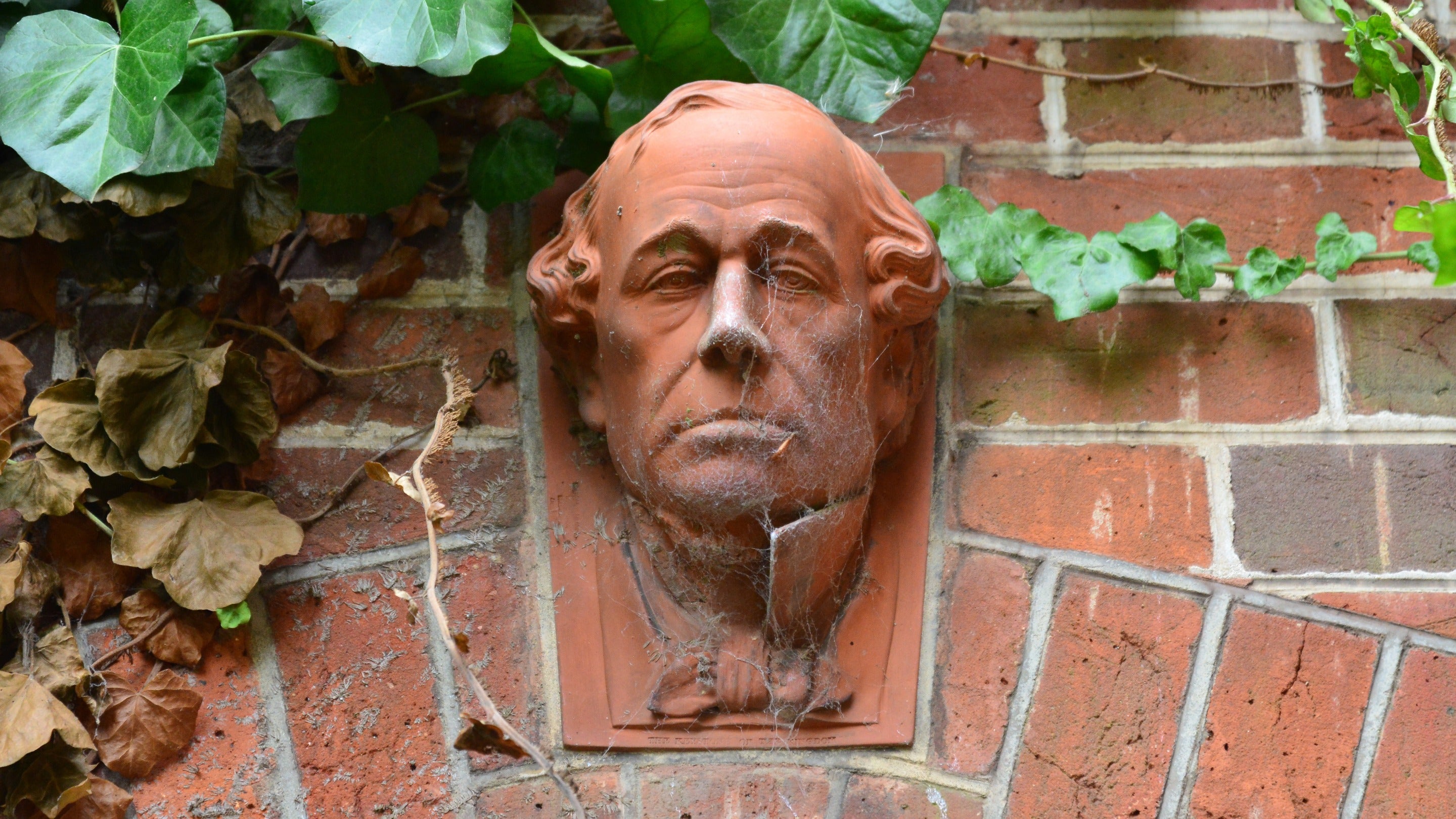 Close up of a sculpture of Disraeli's face in terracotta set into a wall above a doorway with ivy growing around it