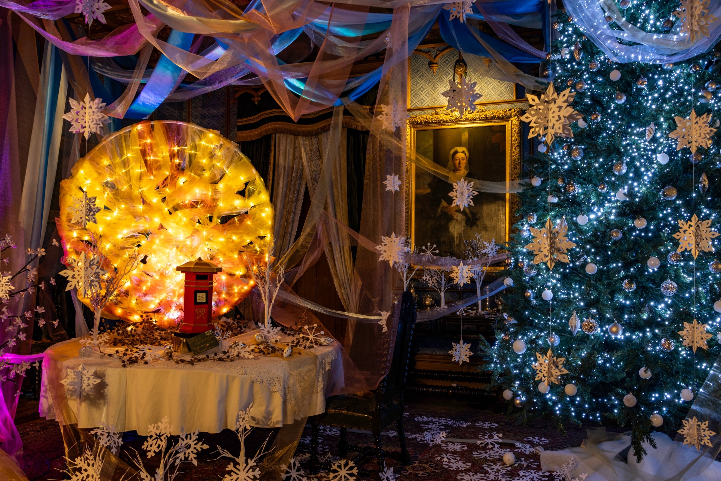 Christmas tree decorated in white lights and snowflakes. The dining room table has a post box and a fabric sun flowing with warm light.