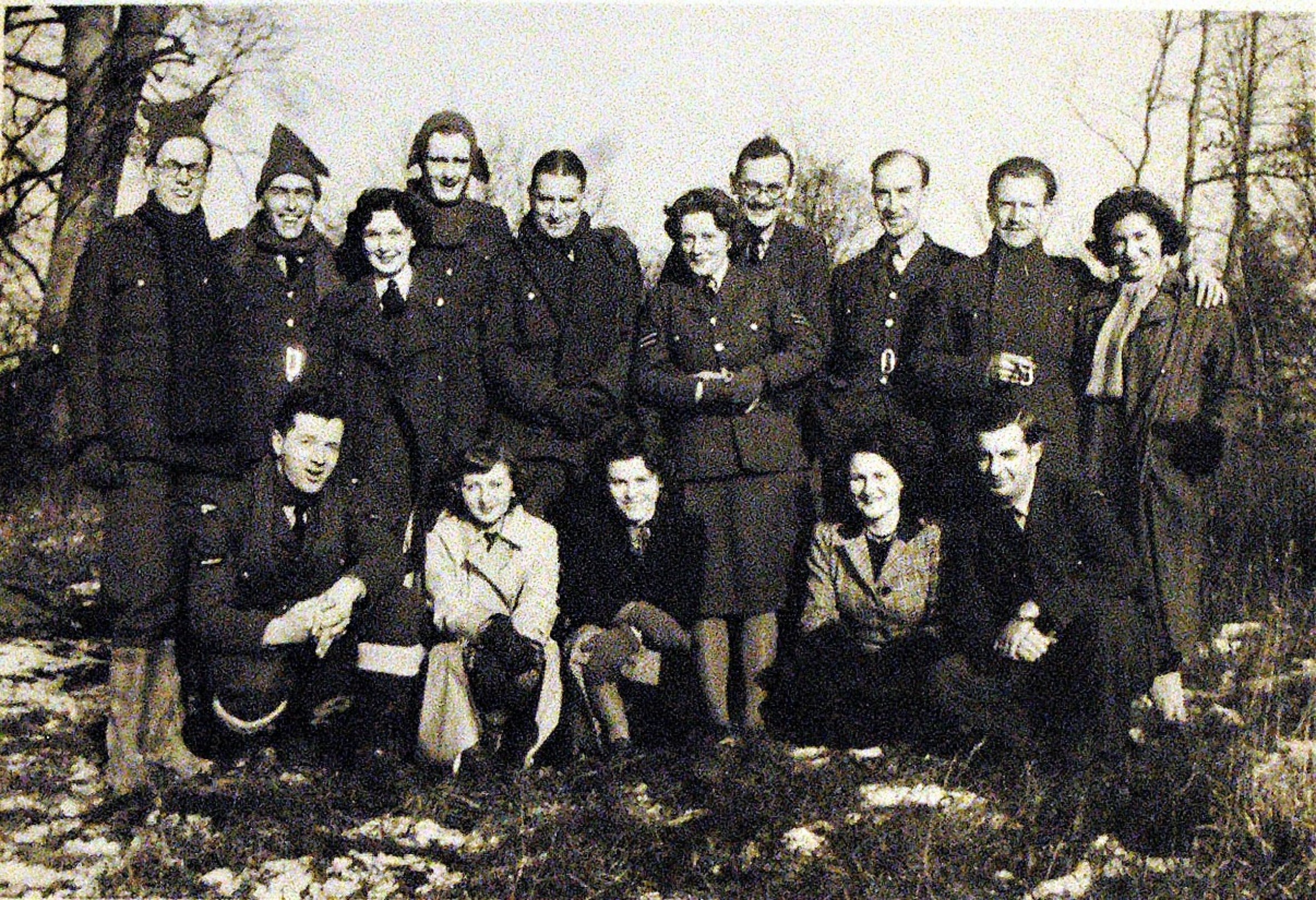 15 men and women in uniform standing and squatting in two rows in a black and white photograph