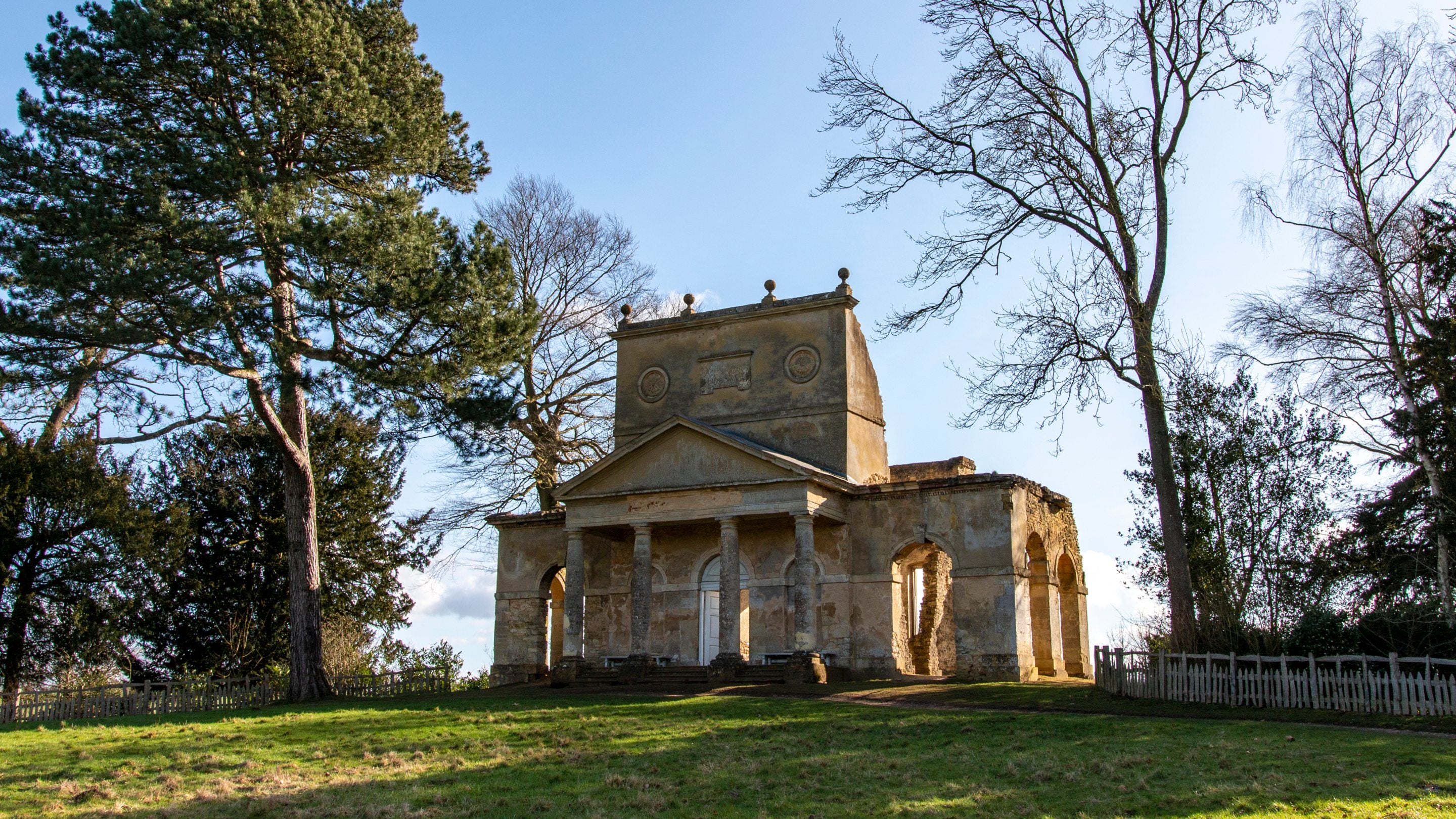 The cream stone Temple of Friendship at Stowe in Buckinghamshire surrounded by greenery and trees