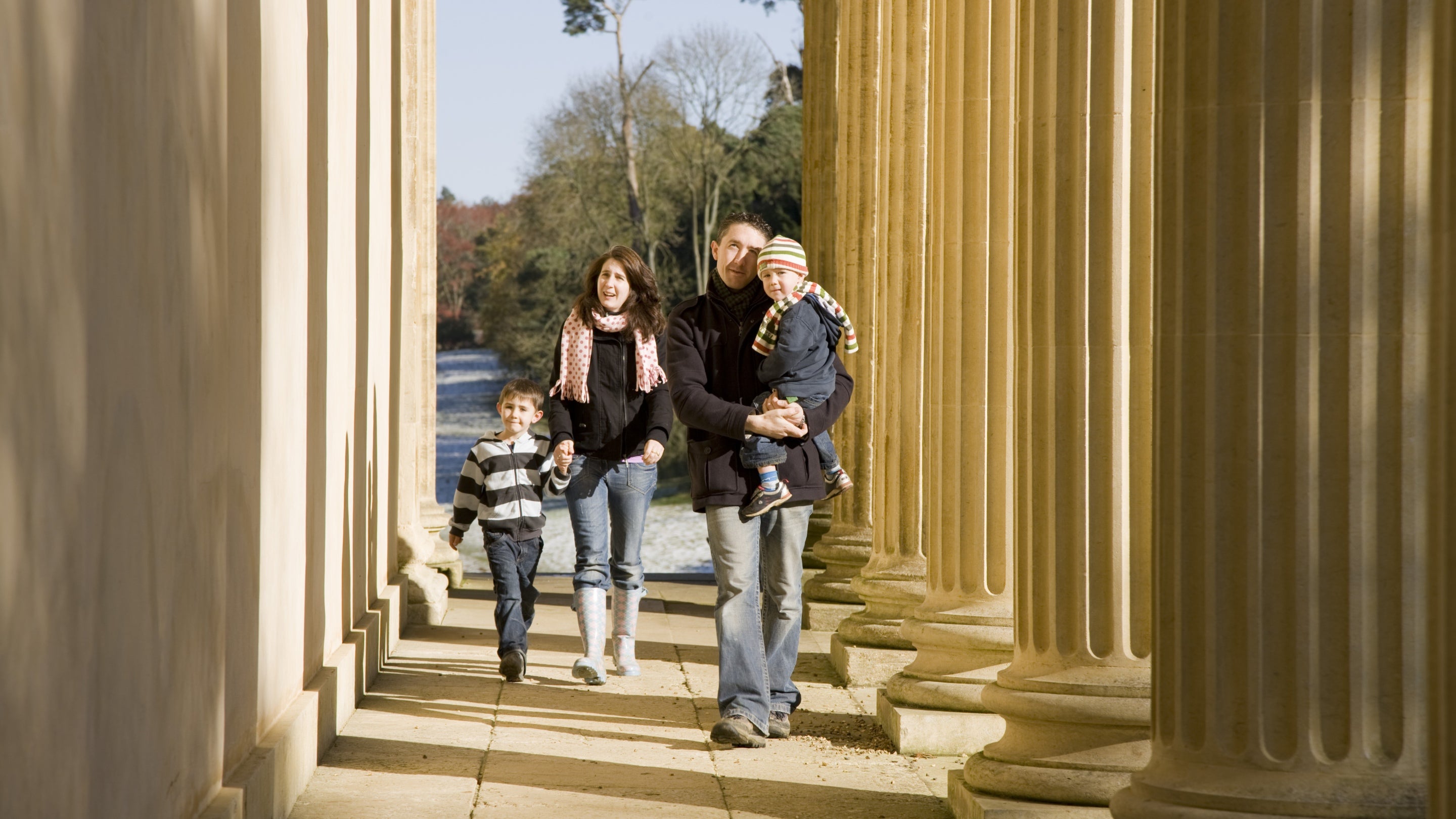 Family dressed for winter walking between the columns of The Temple of Concord and Victory at Stowe Landscape Gardens, Buckinghamshire.