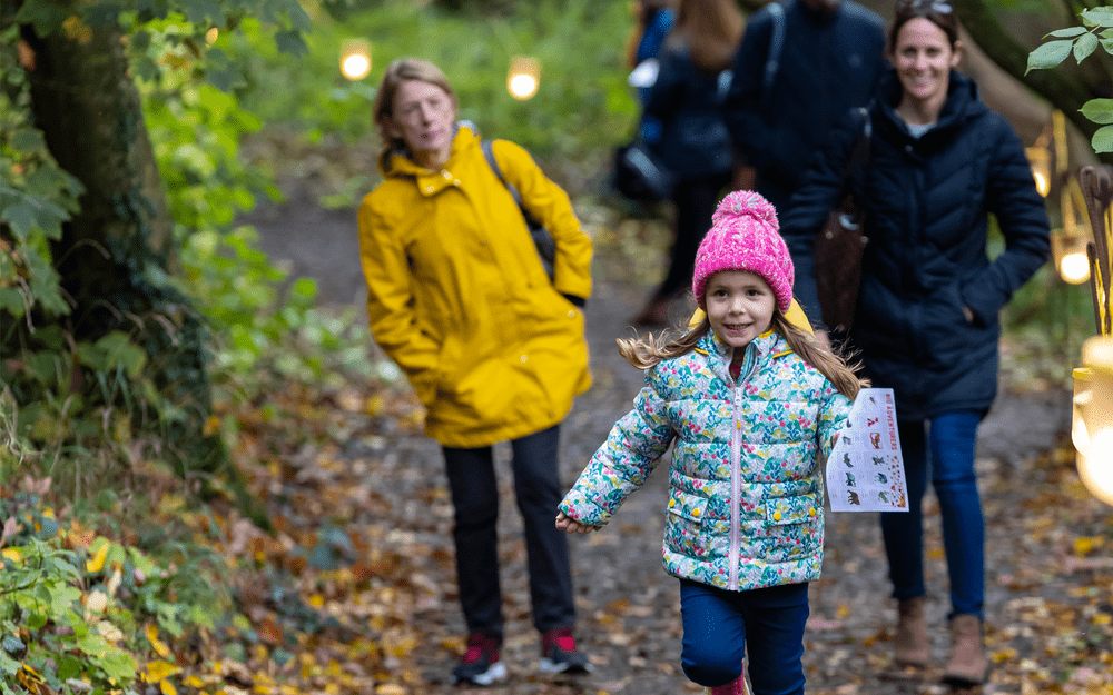 Young girl running through the woods in autumn wearing warm clothing and holding a trail sheet