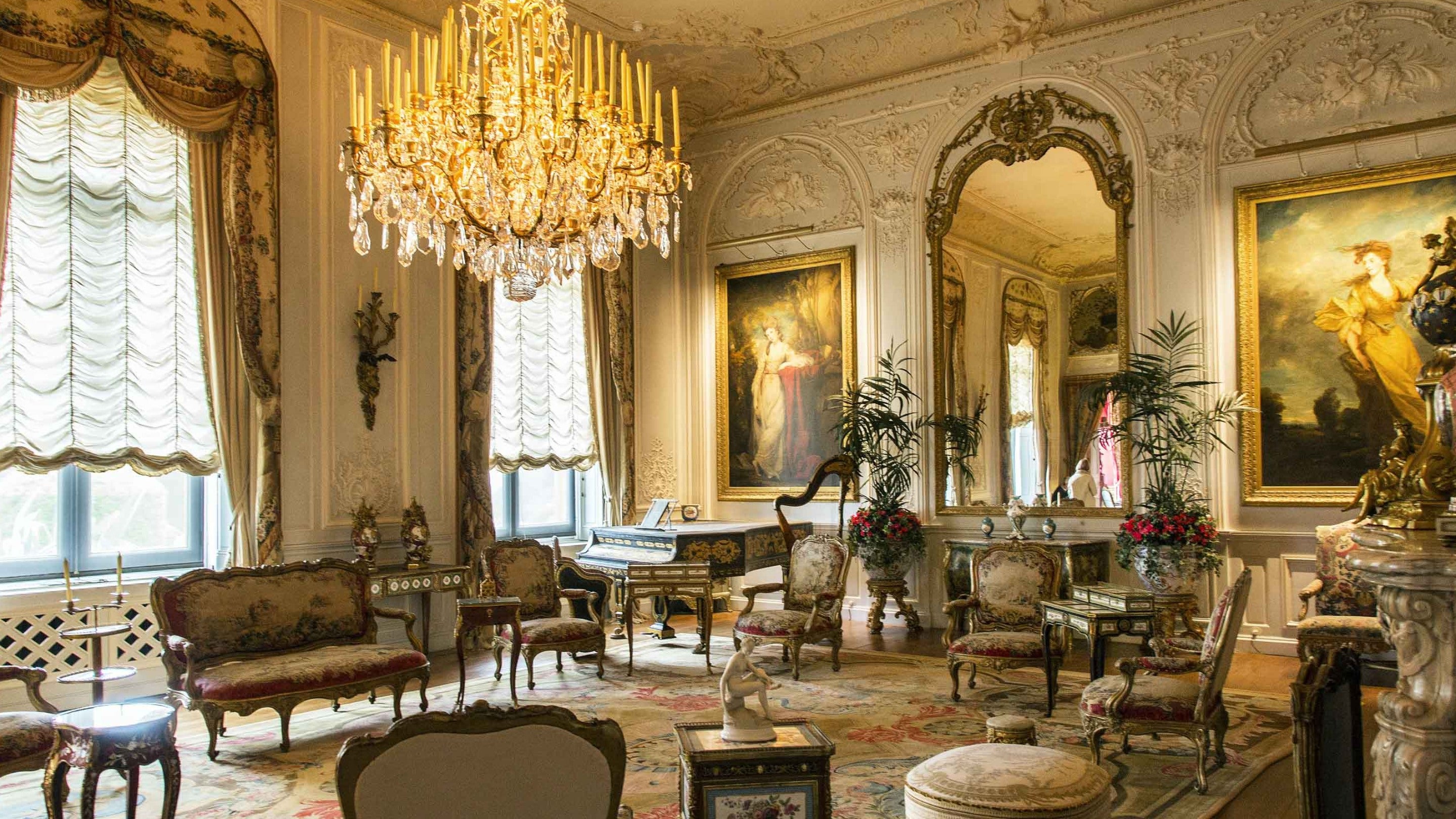 Interior of the Grey Drawing Room at Waddesdon Manor, Buckinghamshire, showing furnishings including chandelier, large mirror, seating and portraits.
