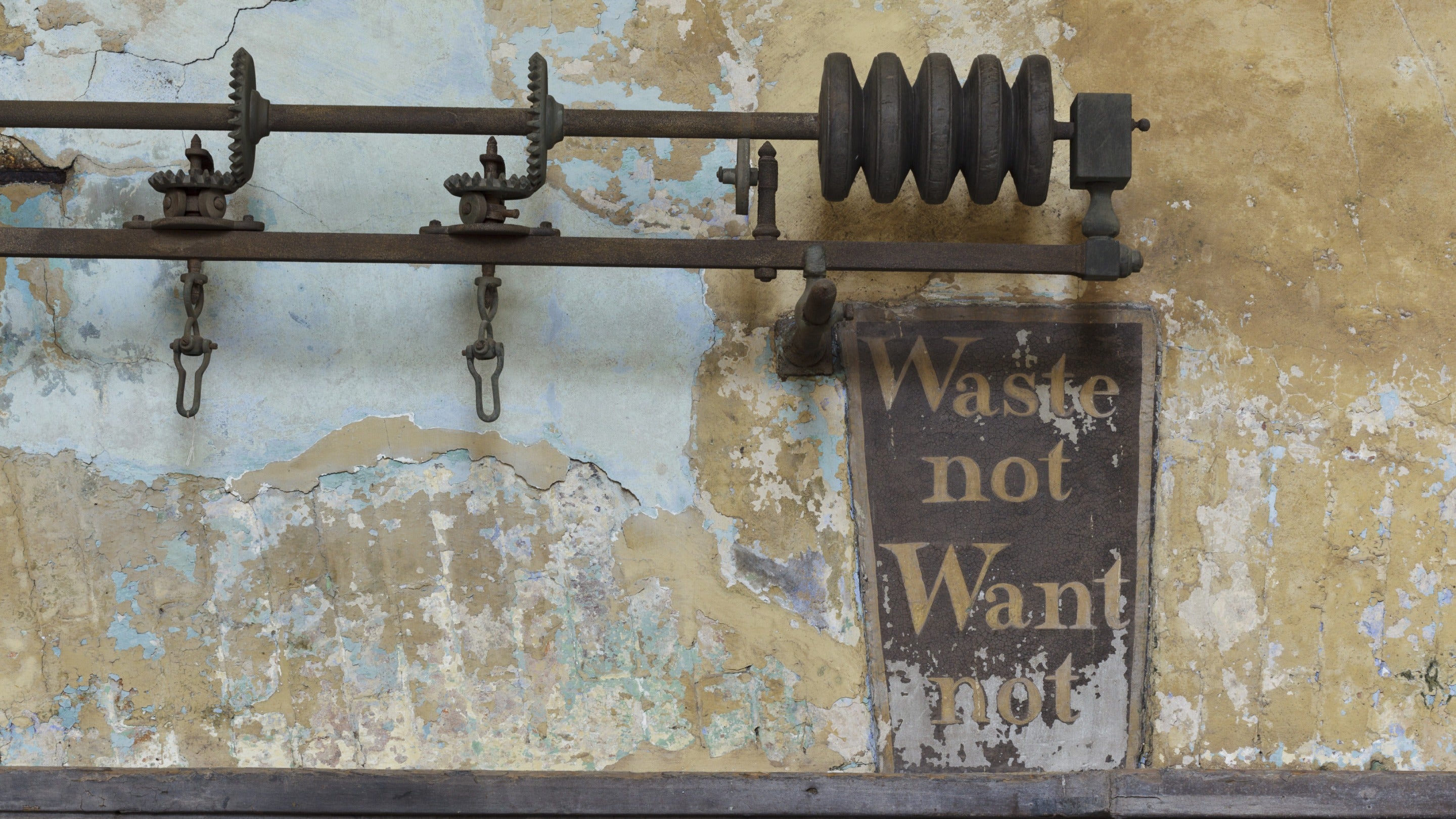 Painted keystone above the fireplace in the Kitchen at Calke Abbey, reading 'Waste not Want not', with peeling plaster behind