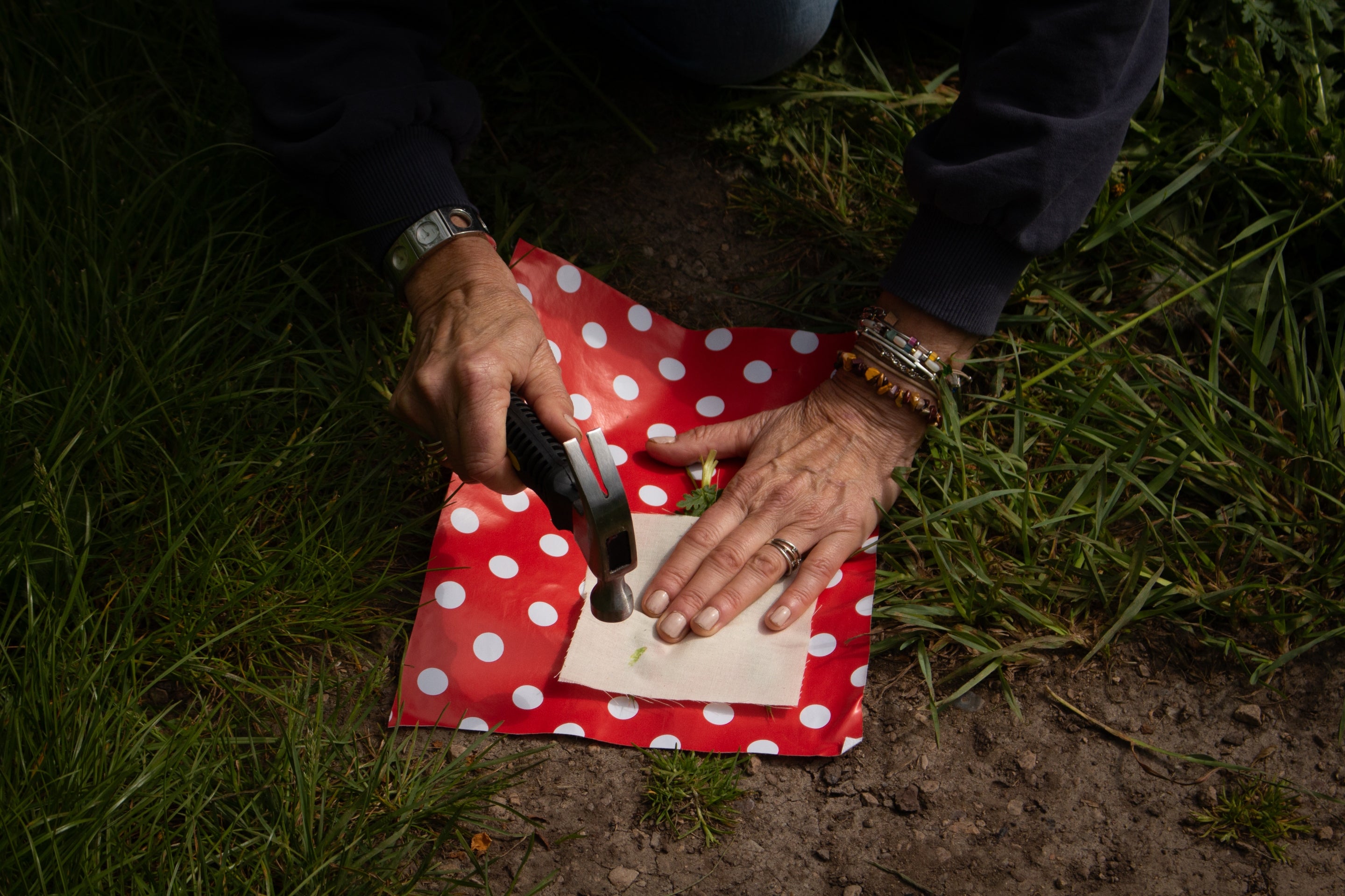 A person using a hammer to create a Hapa Zome print of wild plants onto fabric.