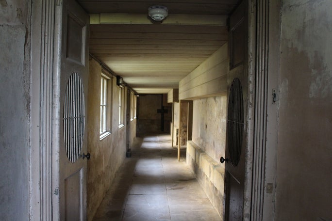 A shadowy stone corridor lit by natural light from windows at equal intervals on the left wall.