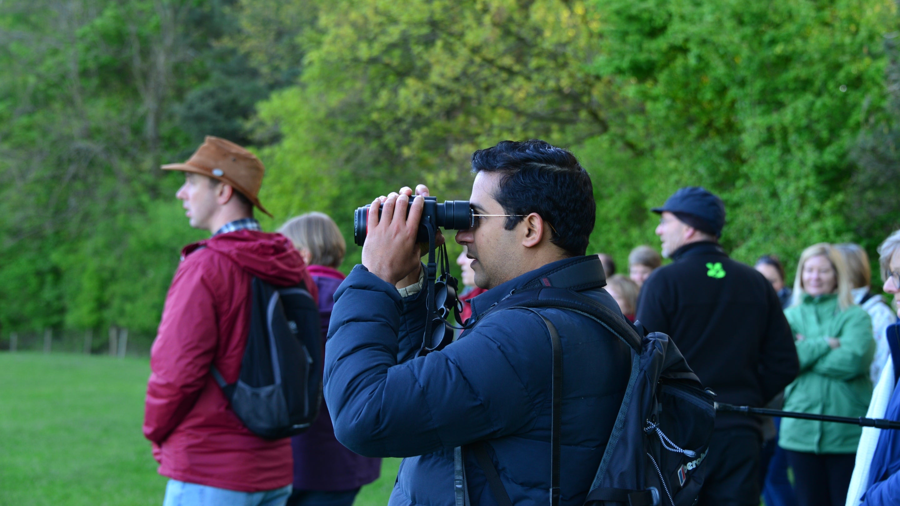 A group of visitors enjoying a dawn chorus guided walk in the park at Calke Abbey, focused on a visitor using a pair of binoculars to see the birds