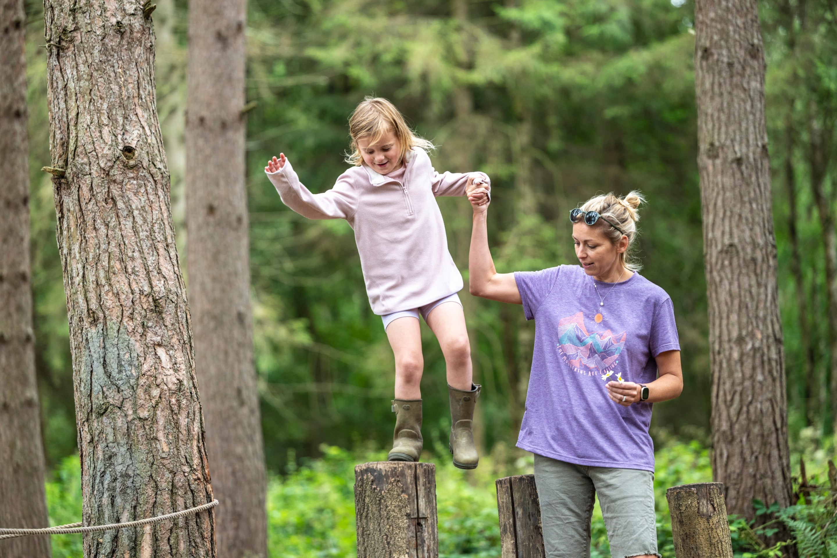 A mother holds her daughter's hand as she balances on logs at the natural play area at Calke Abbey, Derbyshire