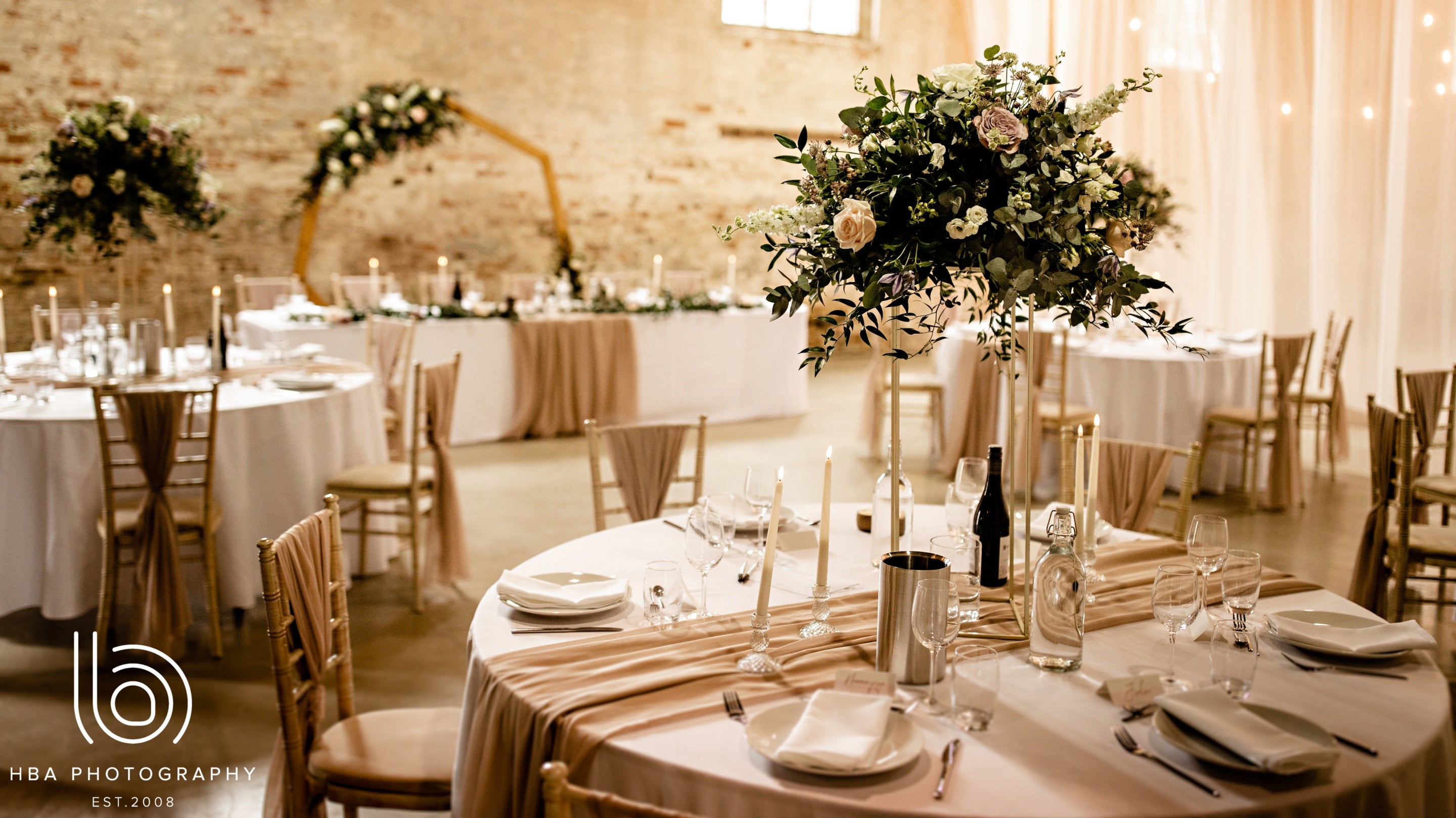 The Riding School at Calke Abbey dressed for a wedding reception, with round tables and tall floral centrepieces