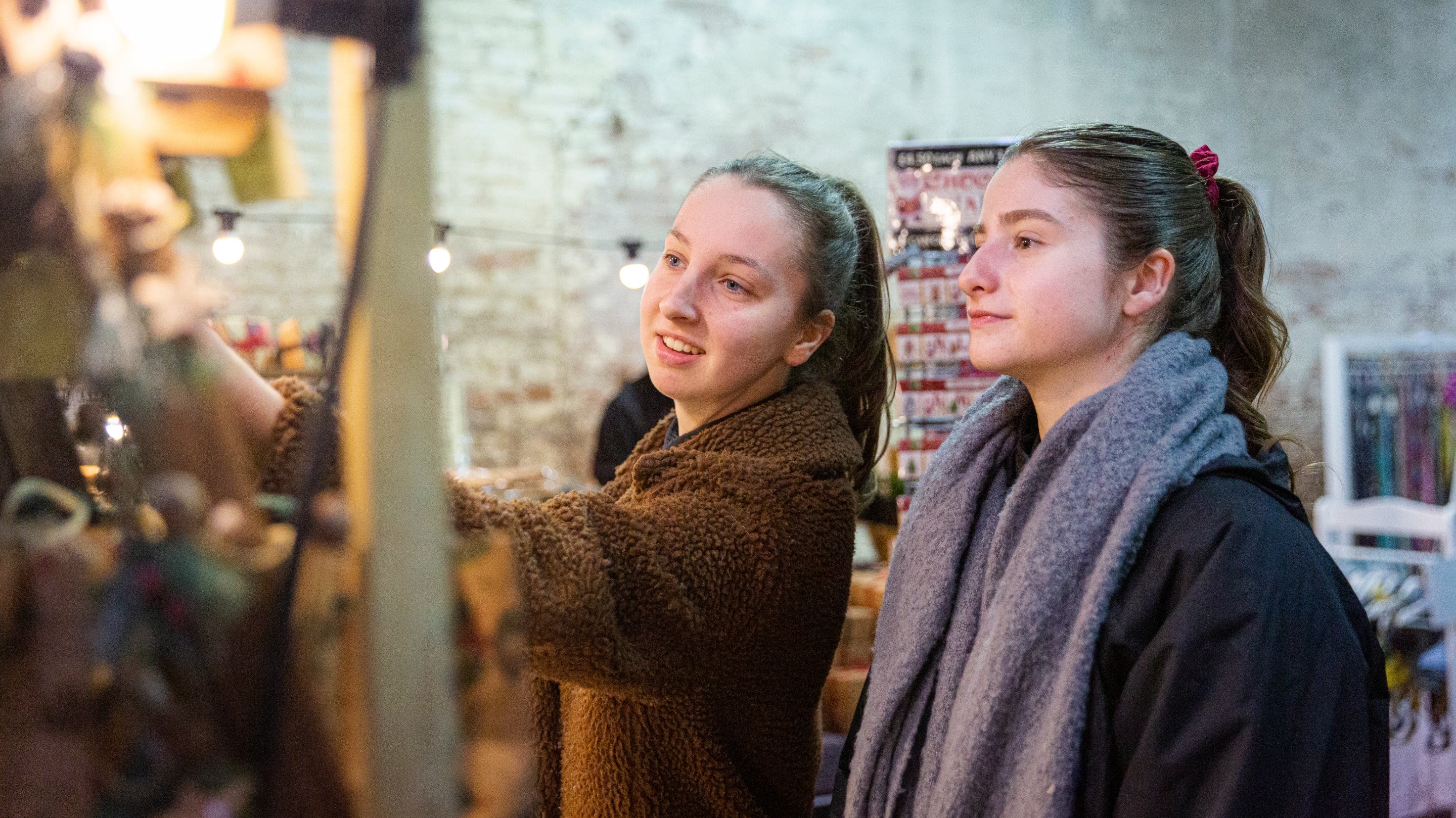 Two women explore the indoor Christmas market at Calke Abbey. They're seen here looking and touching products displayed on one of the stalls.