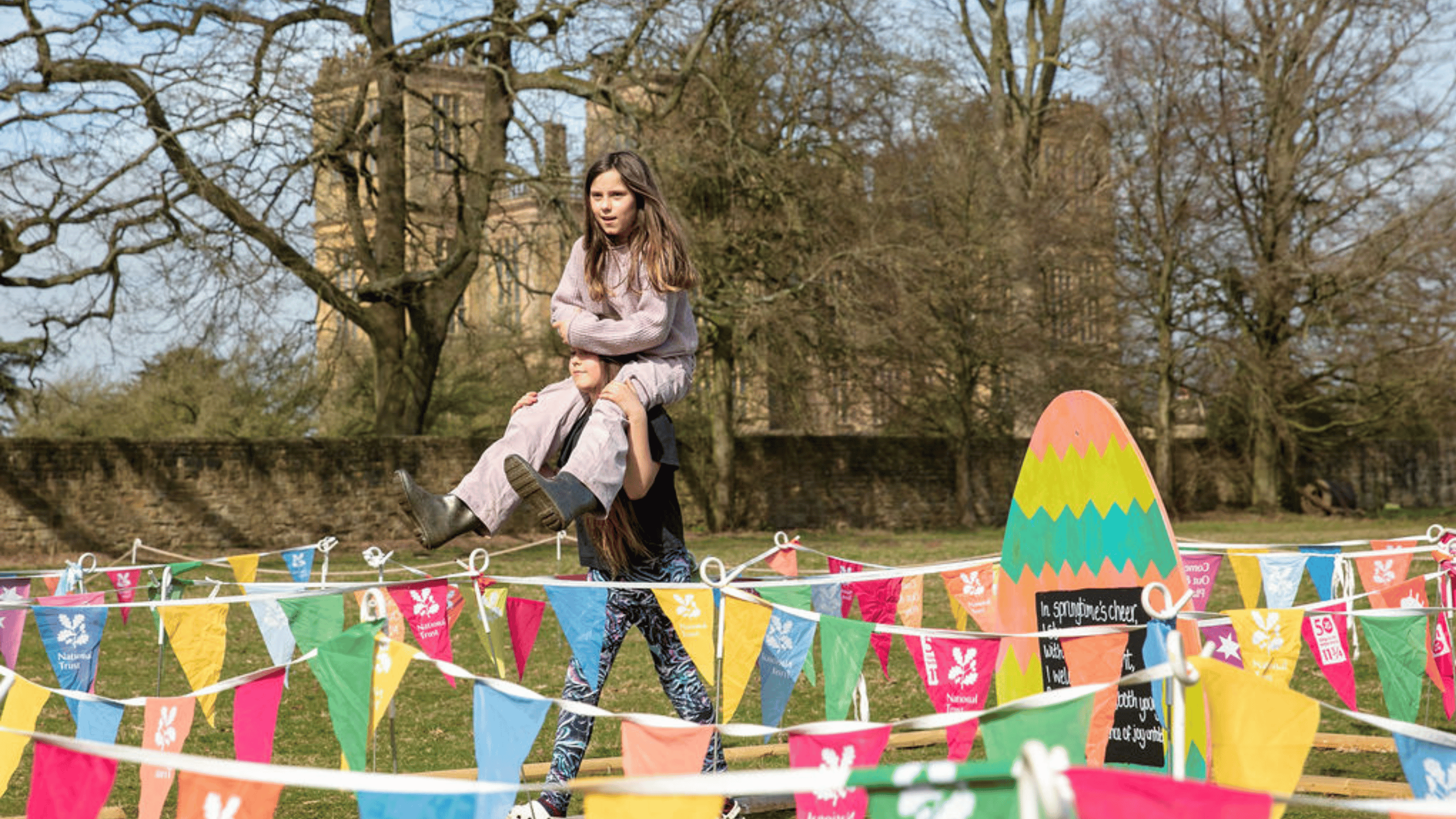 Sister carrying her sister through the bunting maze on her shoulders at Hardwick.