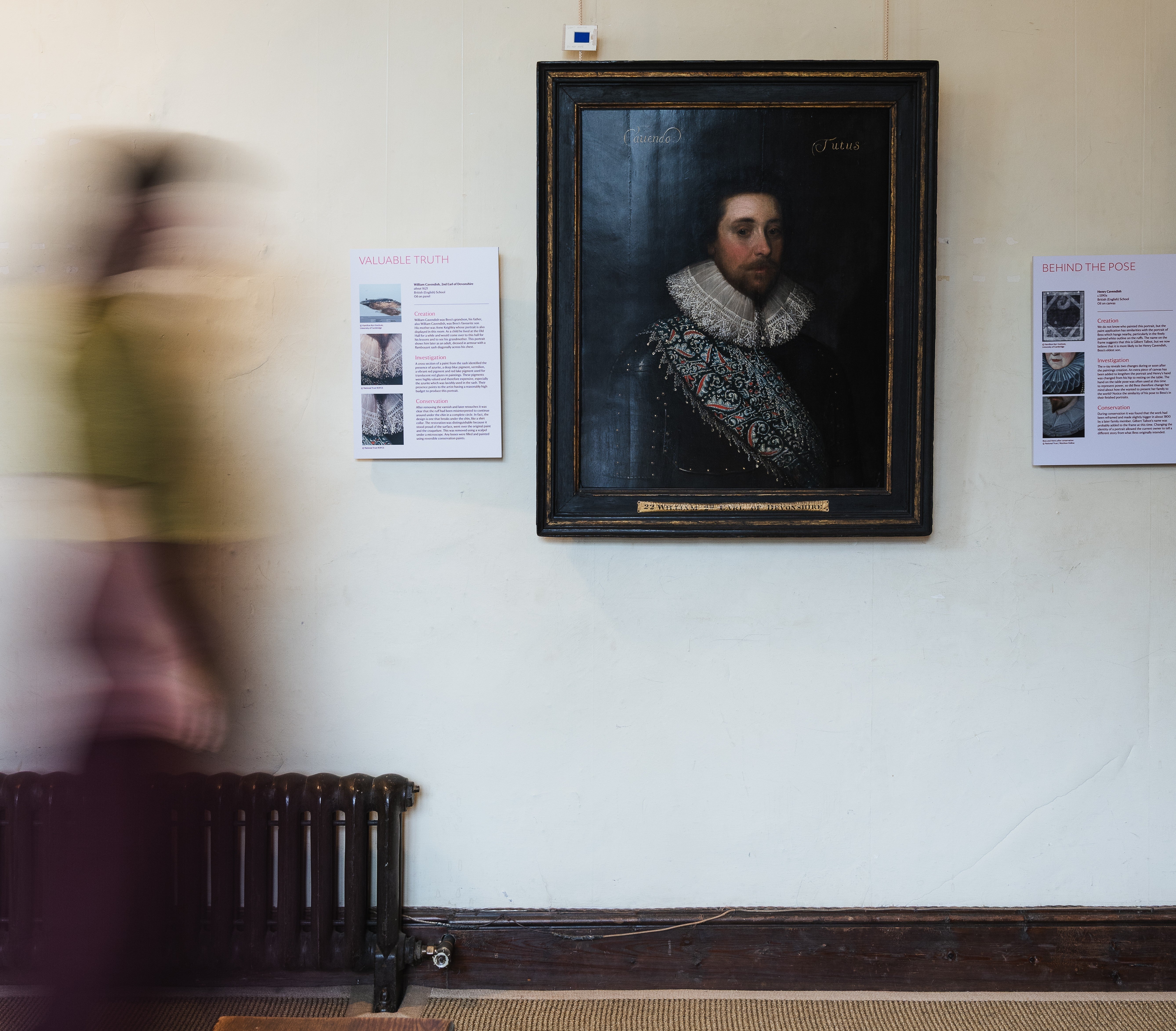 A female visitor walks across an exhibition room in front of the portrait of a gentleman.