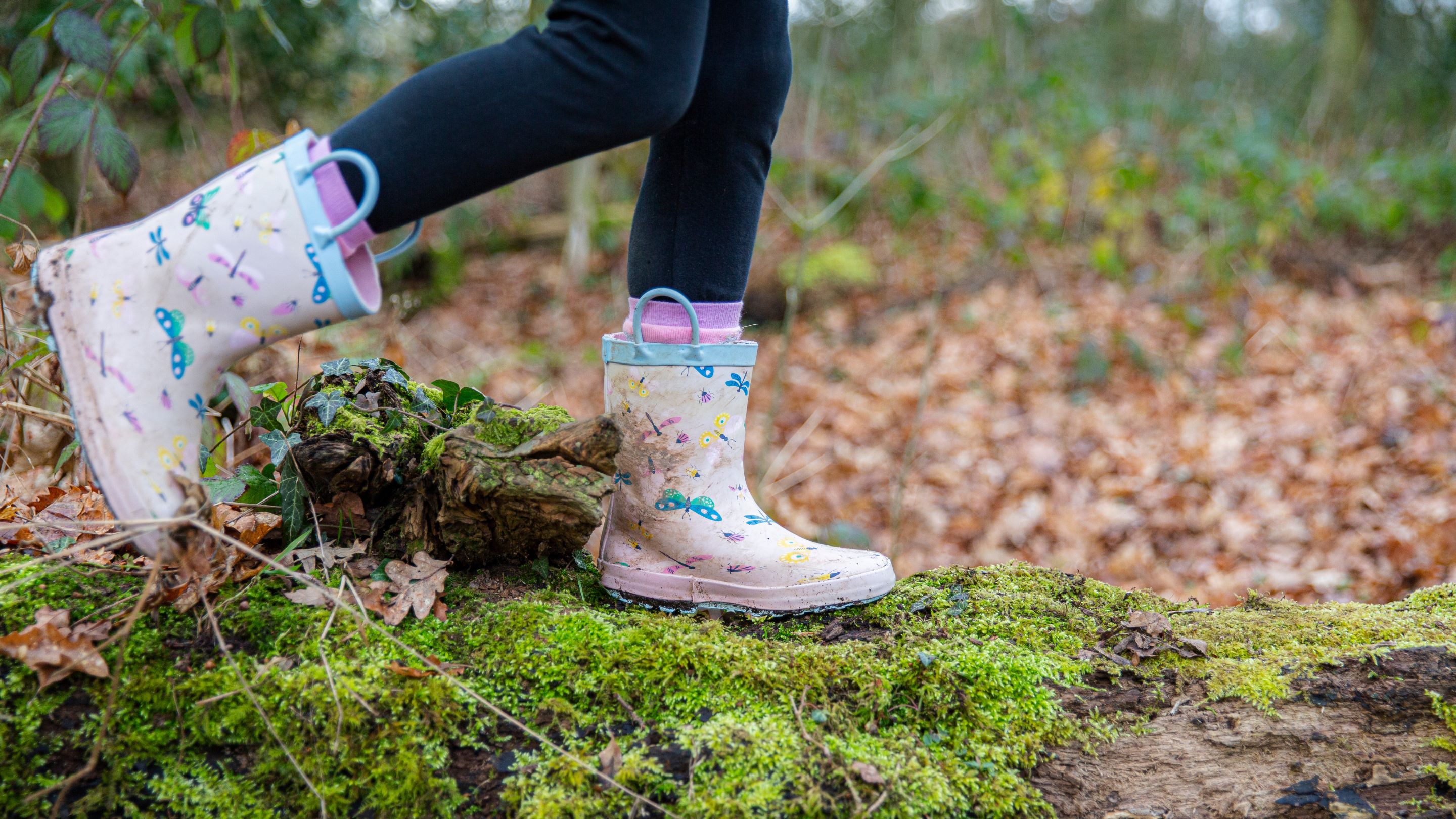Brightly colours girls boots jumping in a muddy puddle.