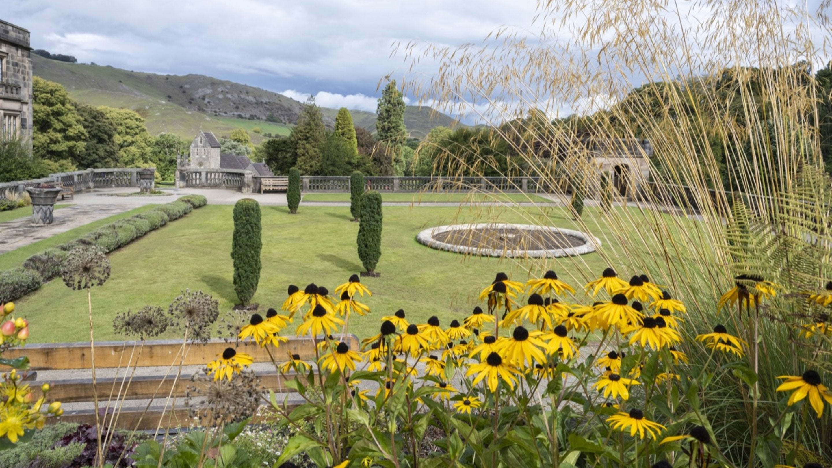 A view over flowers to Italian Gardens at Ilam Park, with a view of a flat topped hill, Thorpe Cloud,  in the background.