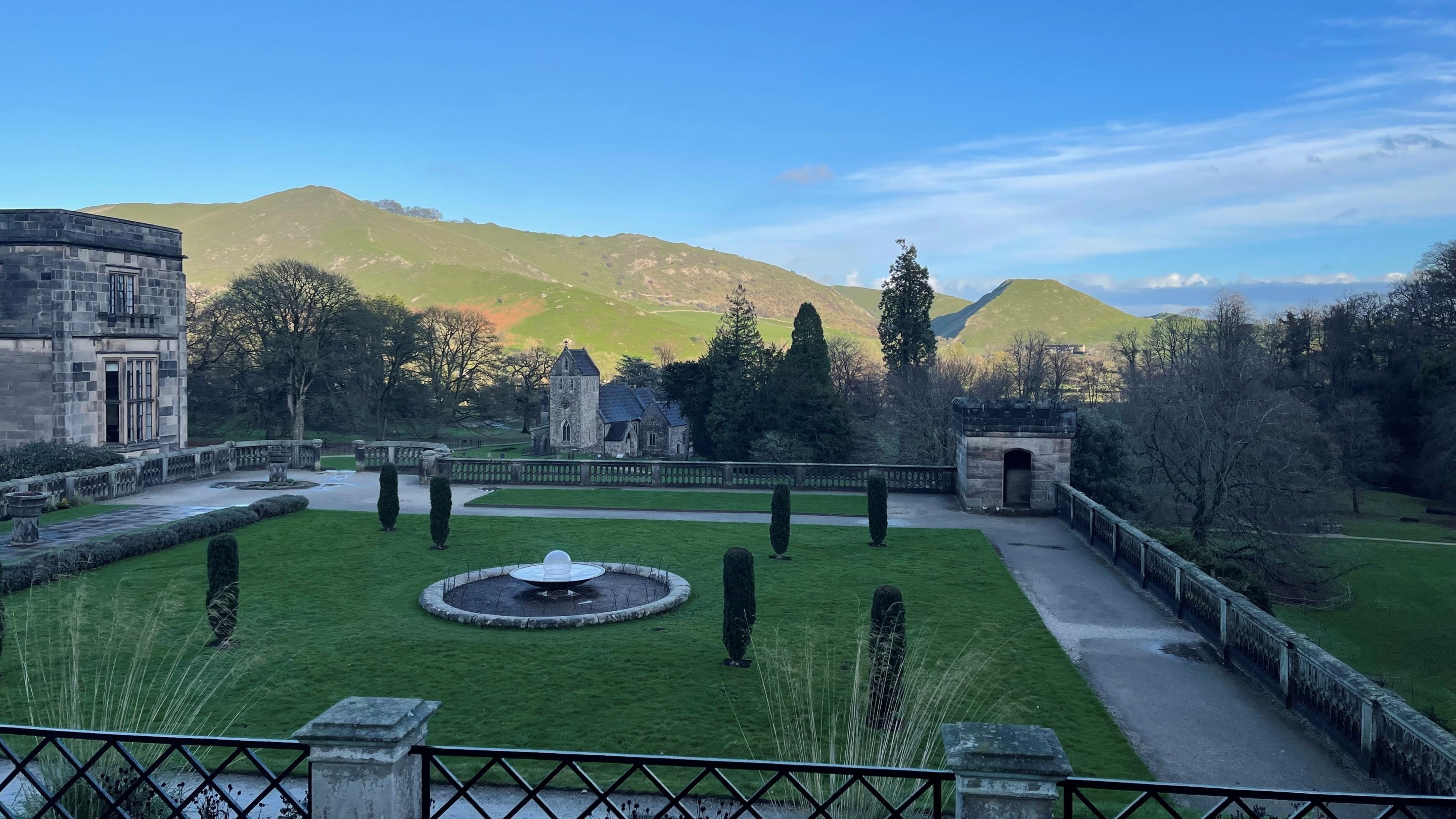 A view over an Italian Garden with a fountain in beneath a flat topped green hill in background