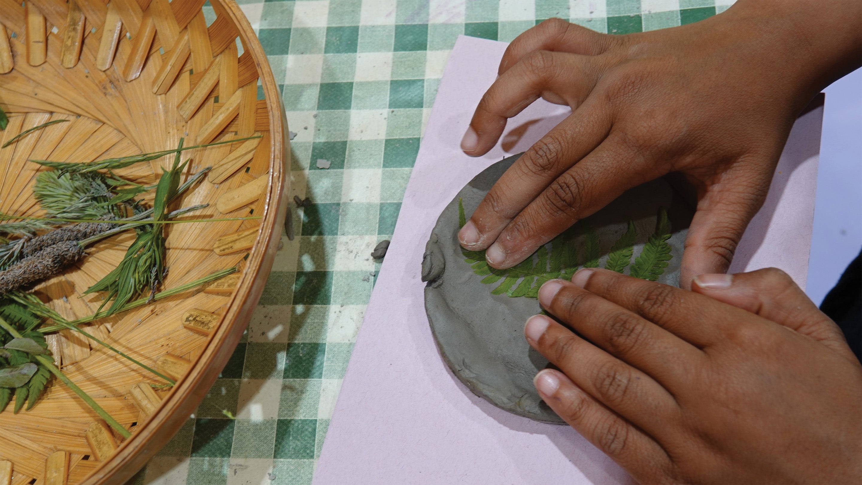 A picture of a child's hands pressing leaves into a clay tile to make a nature inspired print