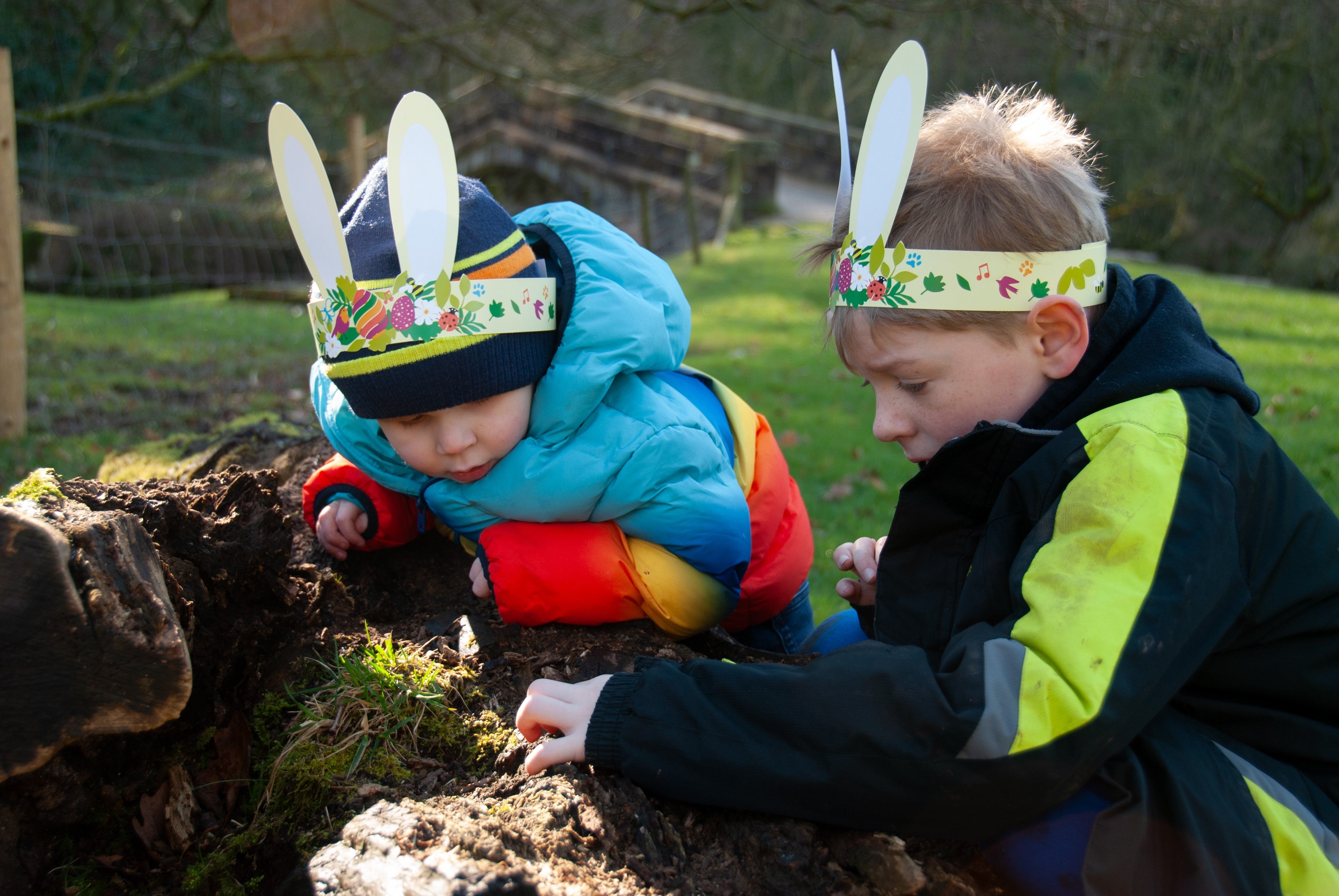Two children wearing bunny ears looking closely at a fallen log