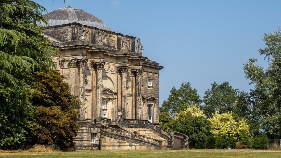 A view looking across the lawn at Kedleston Hall to the house with large trees besides the building