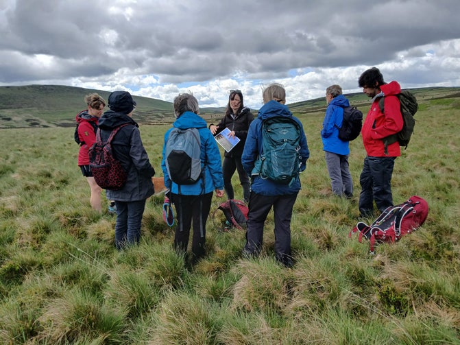 A group of people stood in a circle on a moorland discussing something.