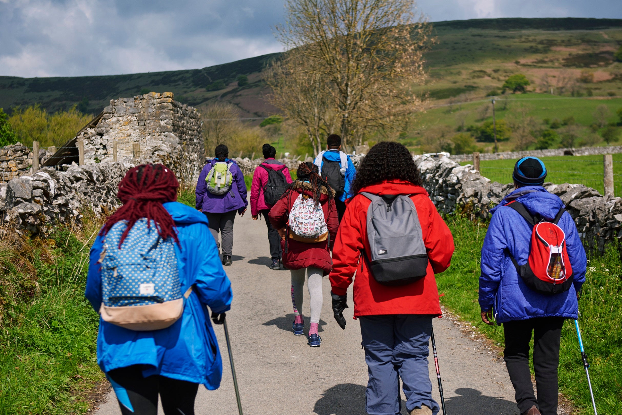 A group of people walking on a path with views of the peak district moors in the background and drystone walls alongside the path
