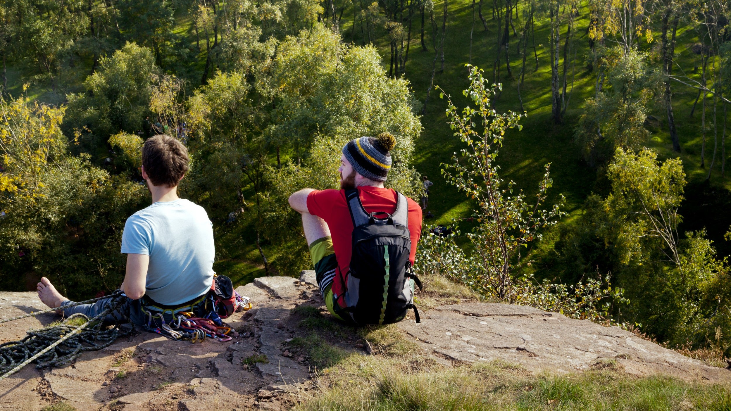 Two climbers sitting on top of cliff overlooking trees