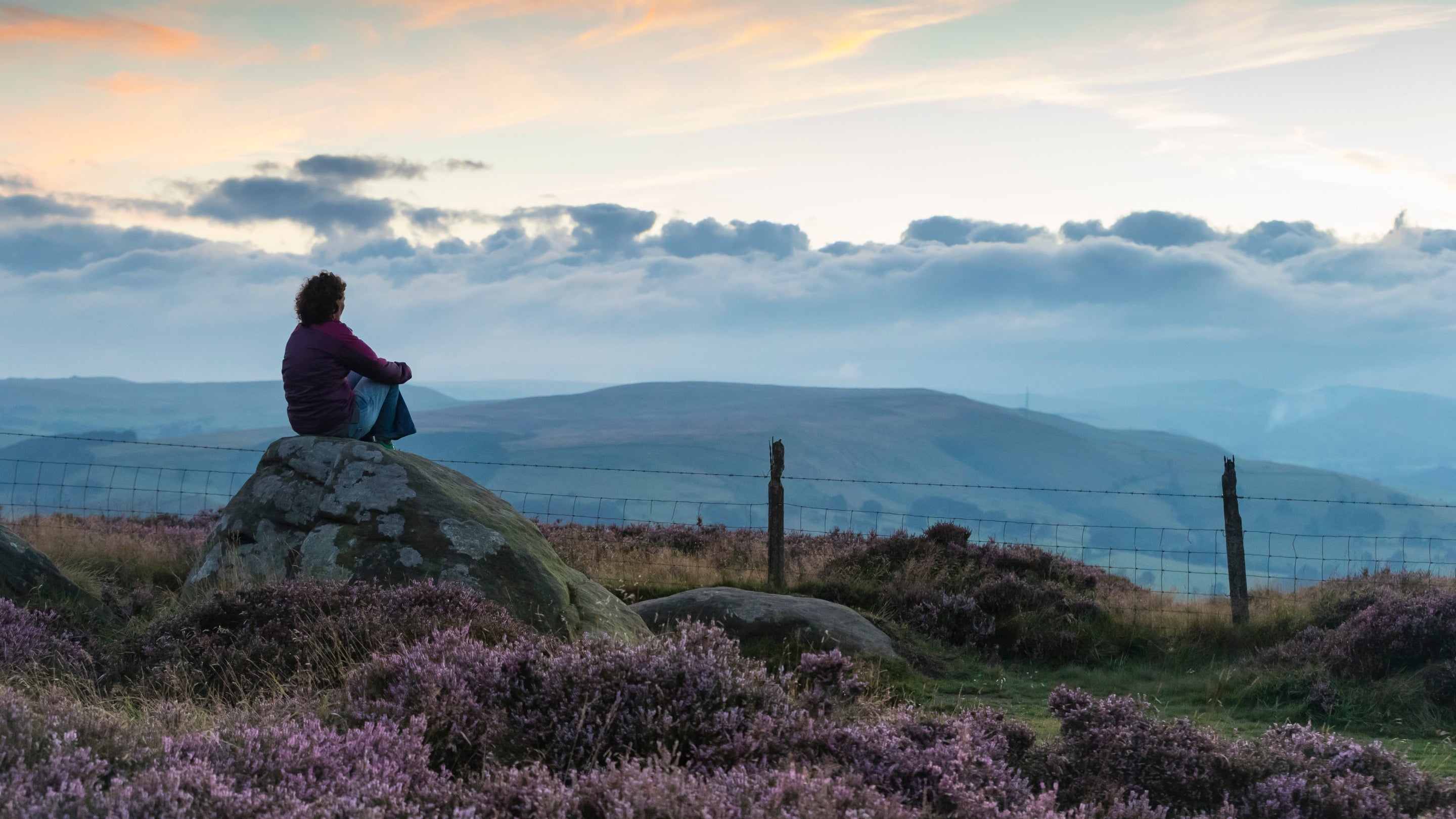 Visitor enjoying the sunset from a rock at Longshaw, Burbage and the Eastern Moors, Derbyshire